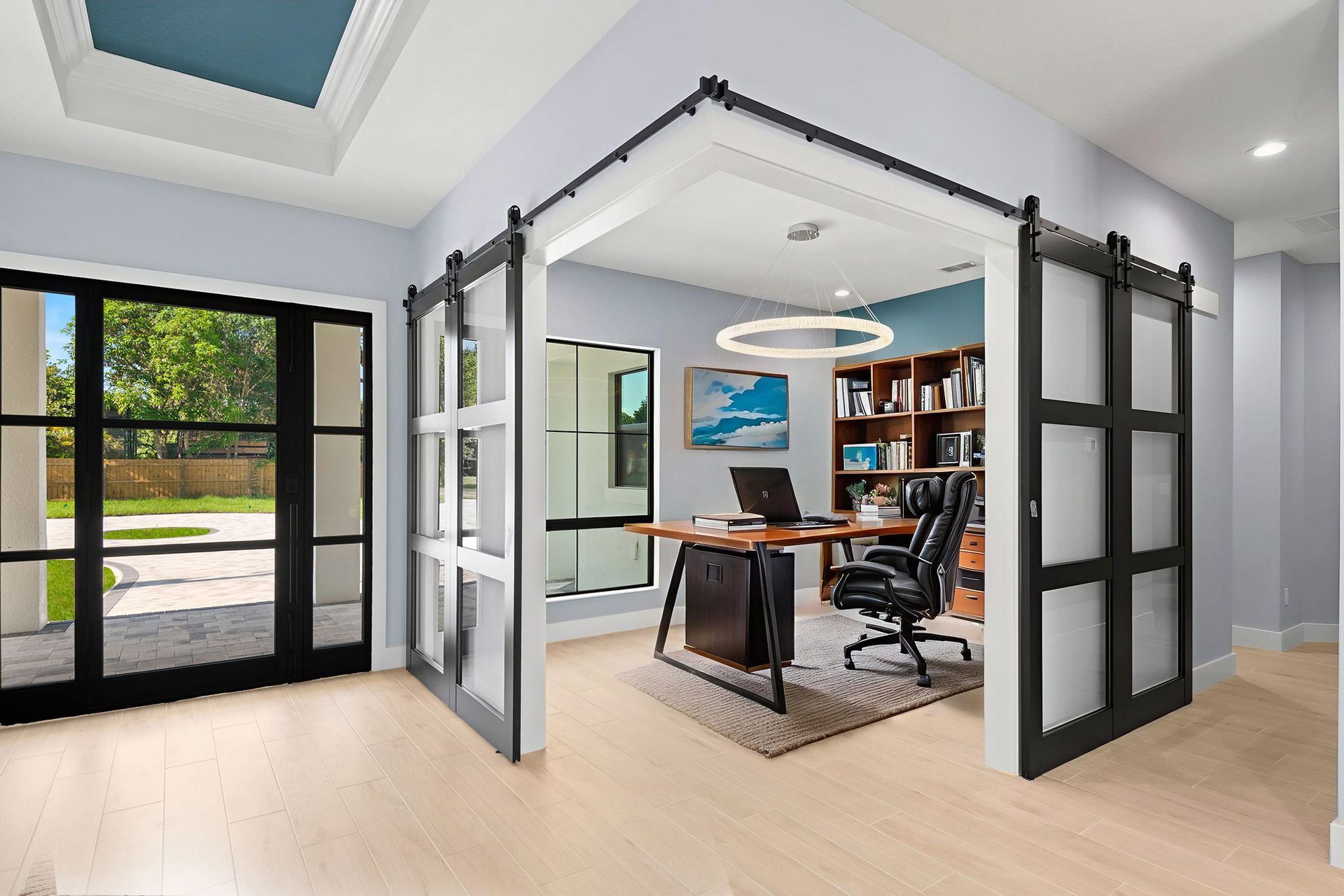 Home office with barn door entry, desk, chair, bookshelves. Light blue walls, light wood floors.