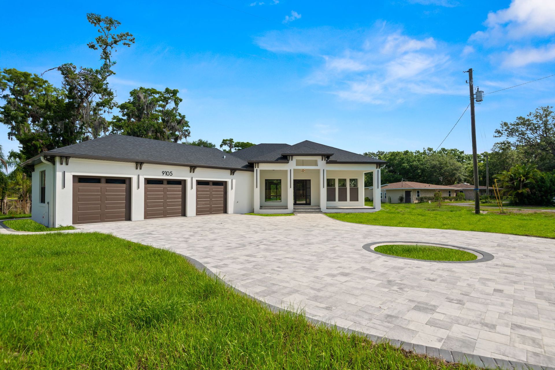 Modern white house with three-car garage, paved driveway, and green lawn under a blue sky.