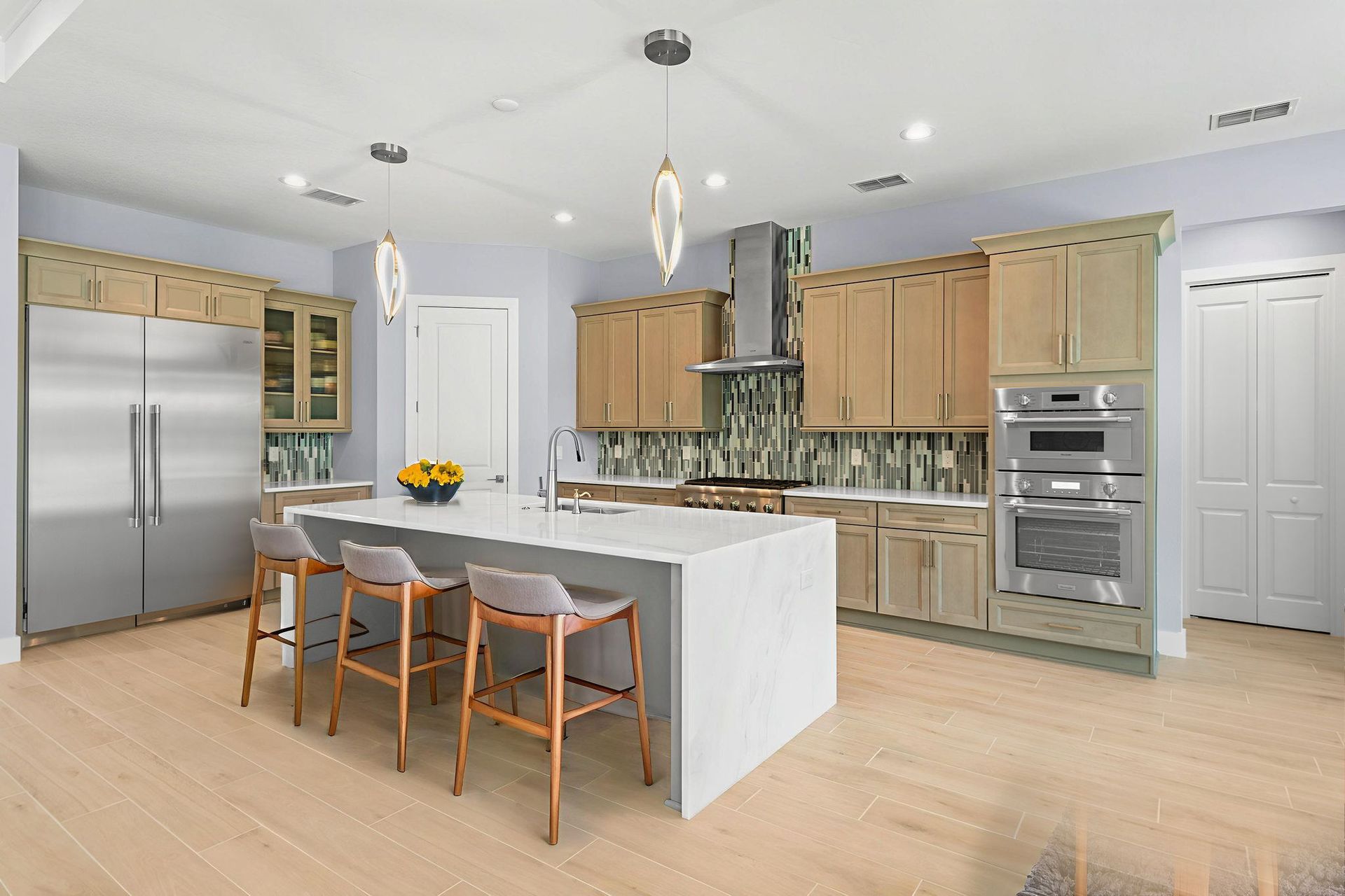 Spacious kitchen with an island, light-colored cabinets, stainless steel appliances, and bar stools on a light wood floor.