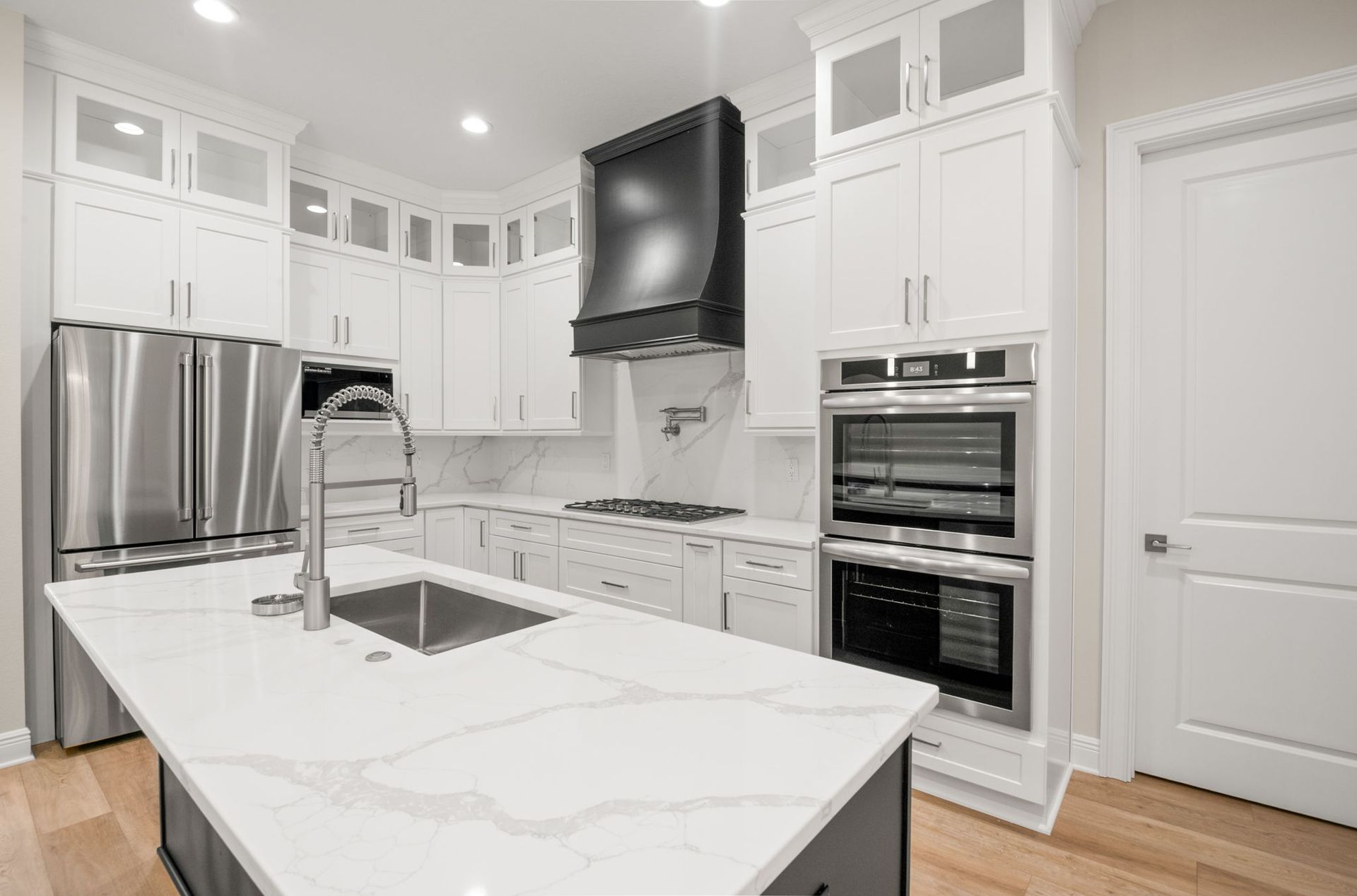 Modern white kitchen with island, stainless steel appliances, and black range hood.