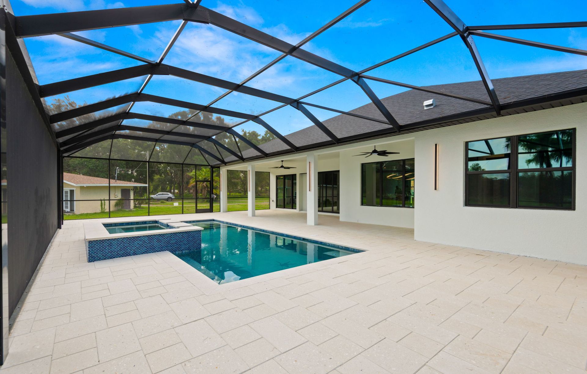 Pool and jacuzzi under a black screened enclosure next to a white house on a sunny day.