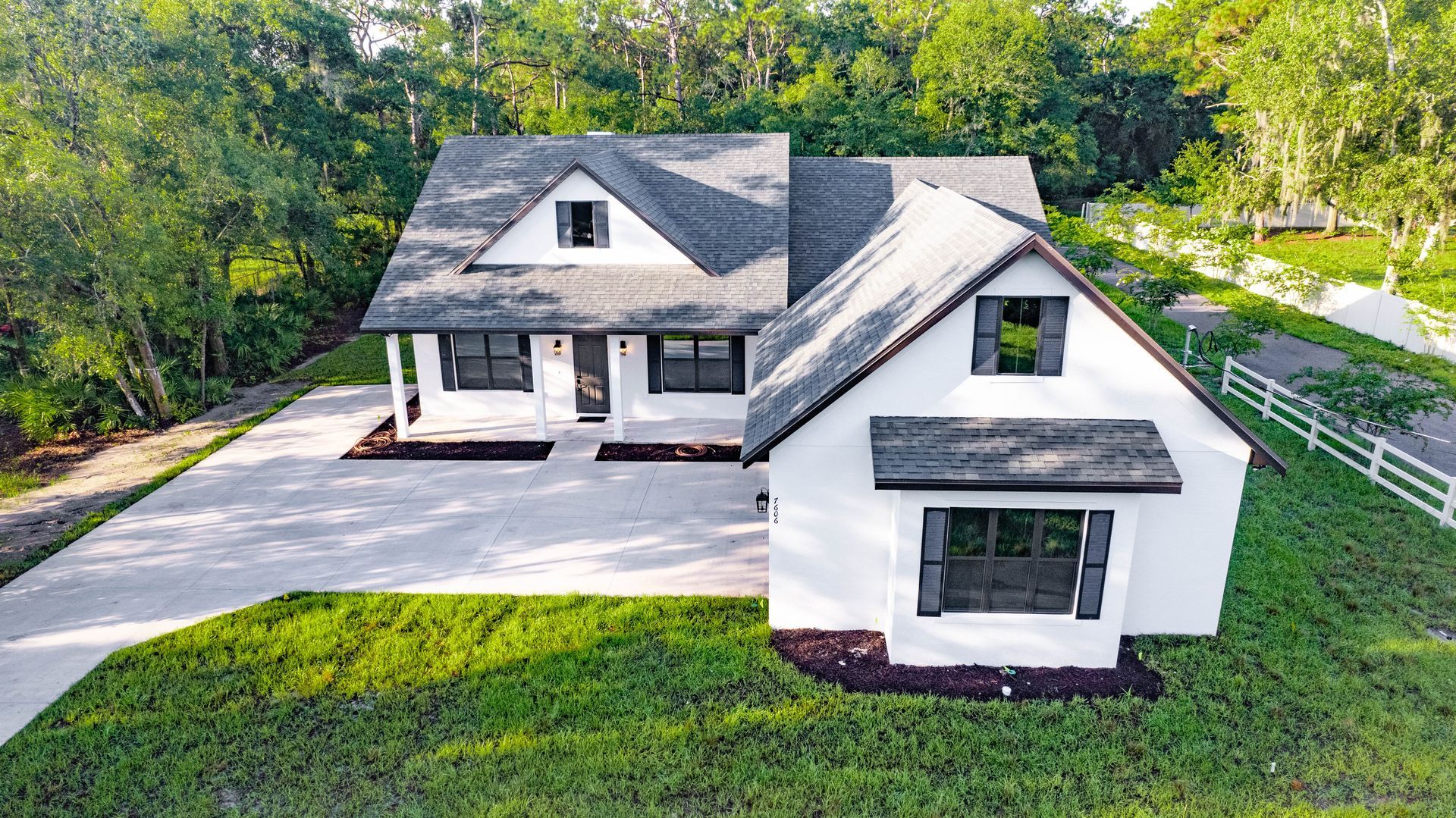 A light green house with a gray roof and brick garage doors on a green lawn with trees.