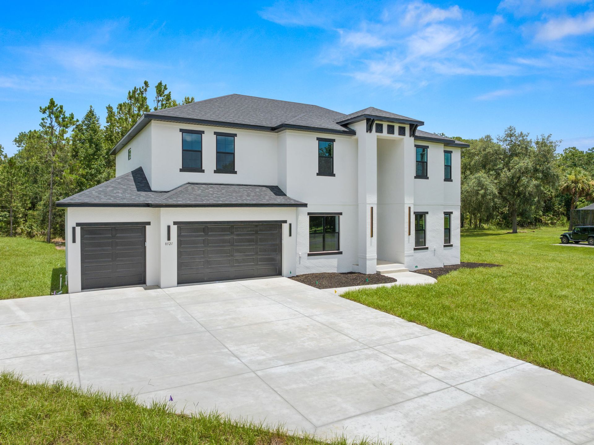 Two-story white house with gray roof and garage doors. Concrete driveway and green lawn.