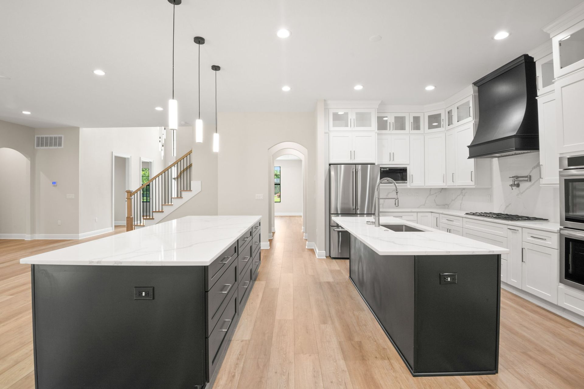 Modern kitchen with two black islands, white counters, and stainless steel appliances.