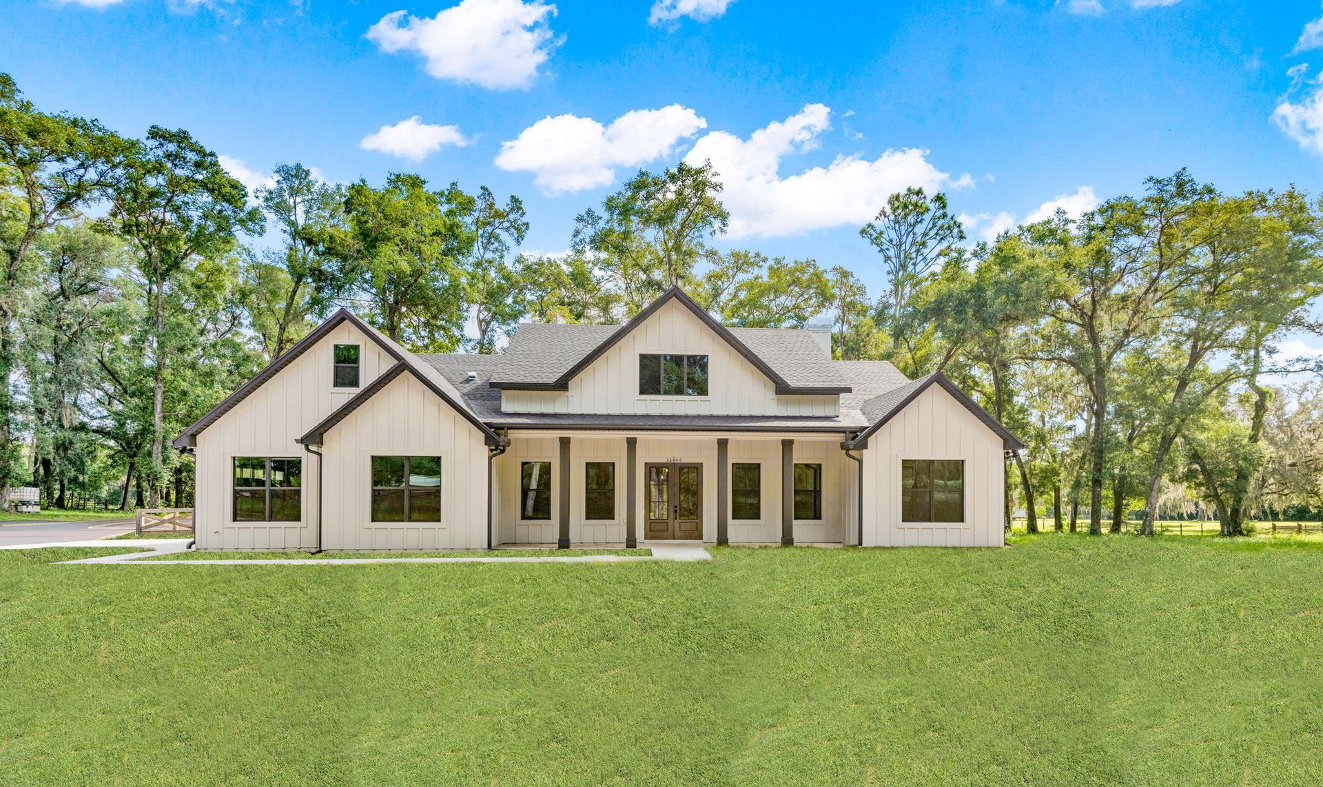 White farmhouse-style home with black trim against a green lawn and blue sky.