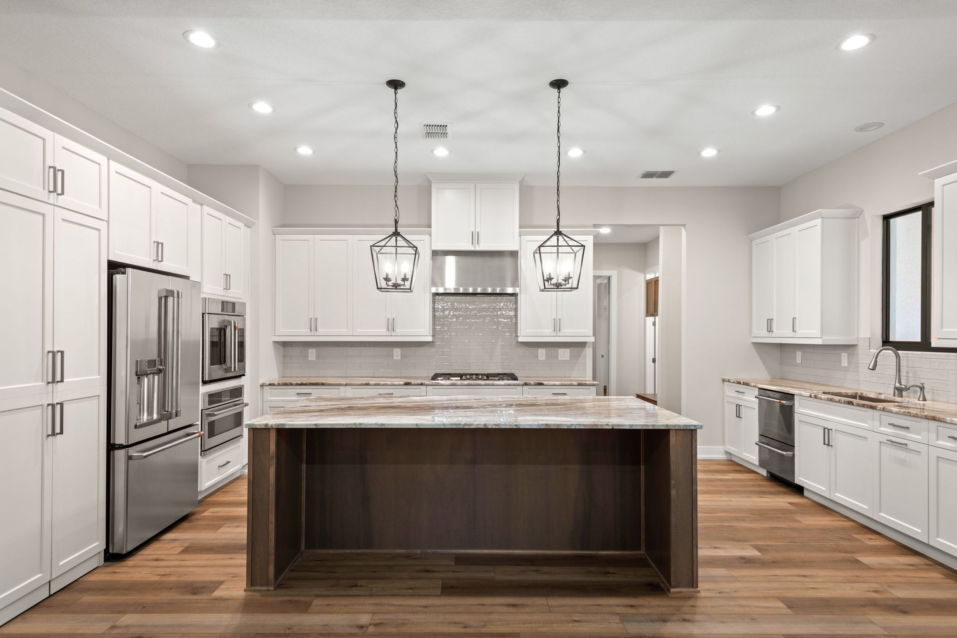 Modern white kitchen with island, stainless steel appliances, and pendant lights.