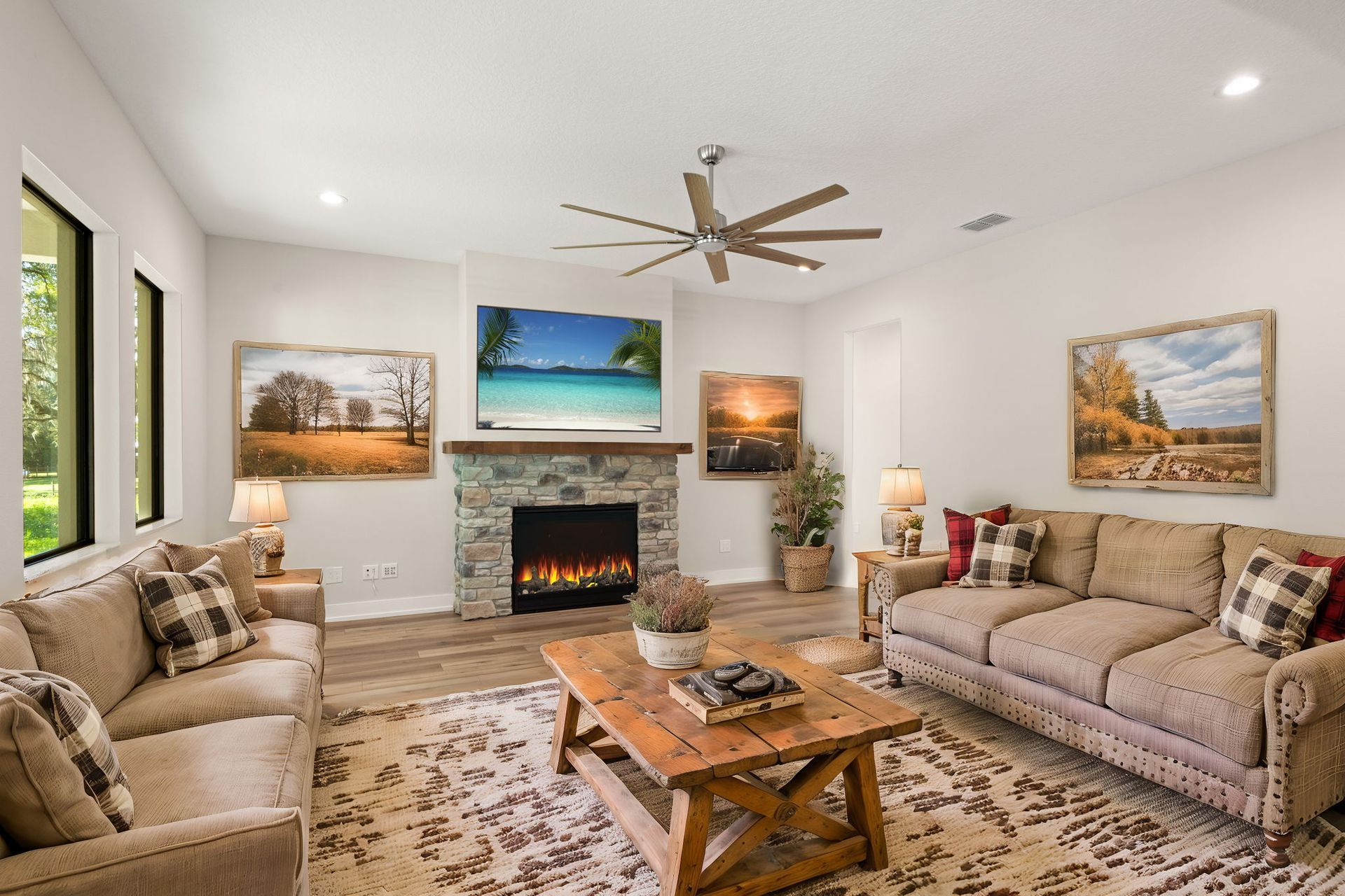 Cozy living room with couches, stone fireplace, landscape art, and ceiling fan.