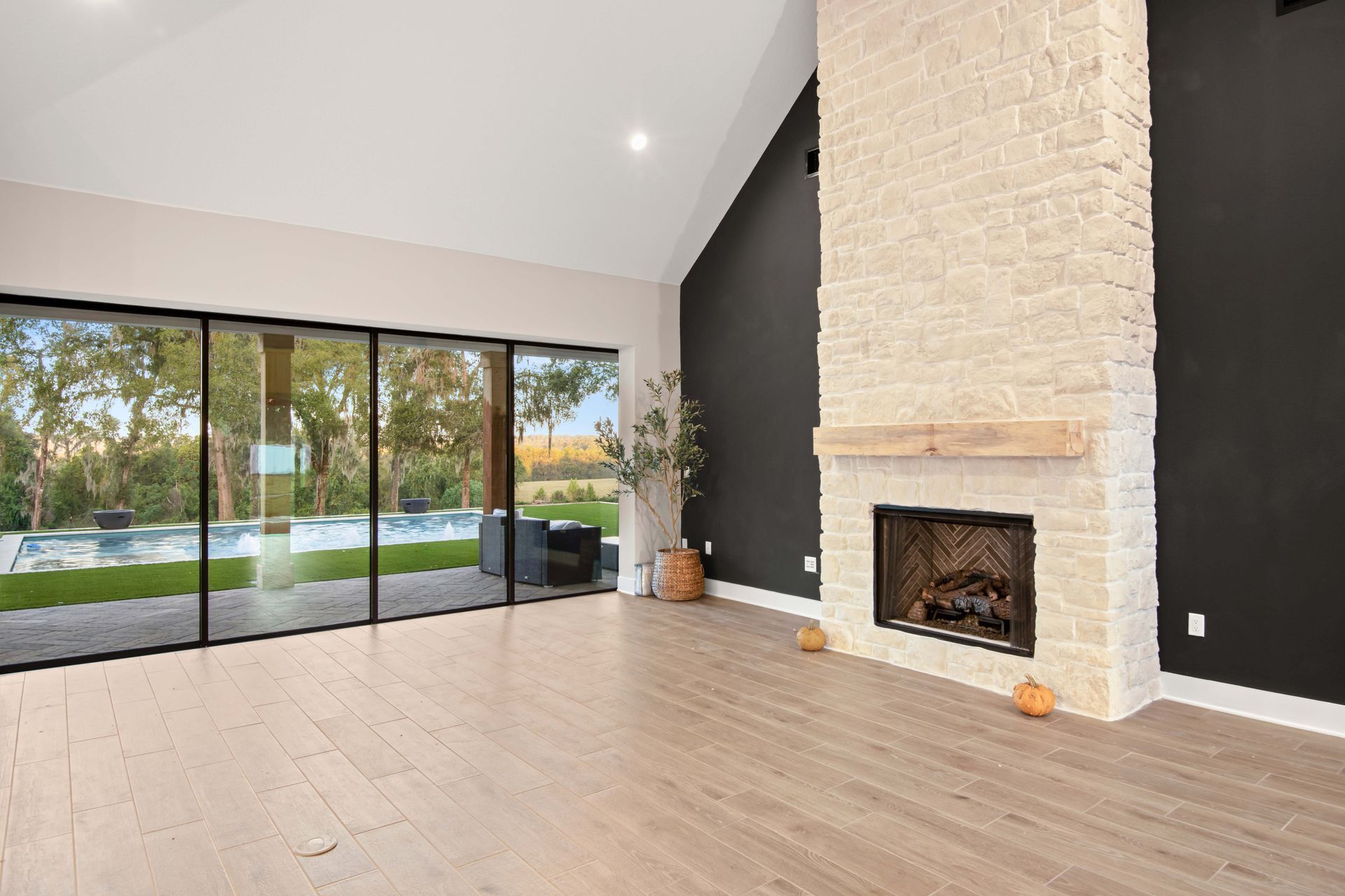 Empty living room with fireplace, large windows overlooking a pool, and hardwood floors.