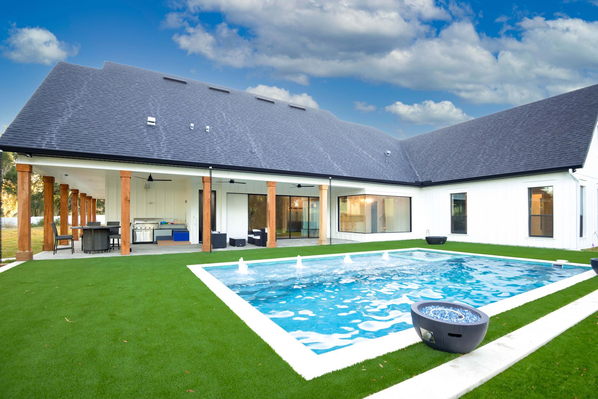 Backyard with pool, white house, green lawn, and blue sky.