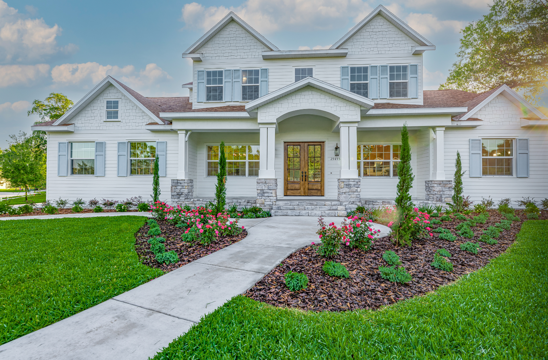 Two-story white house with blue shutters, a landscaped yard, and a concrete walkway.