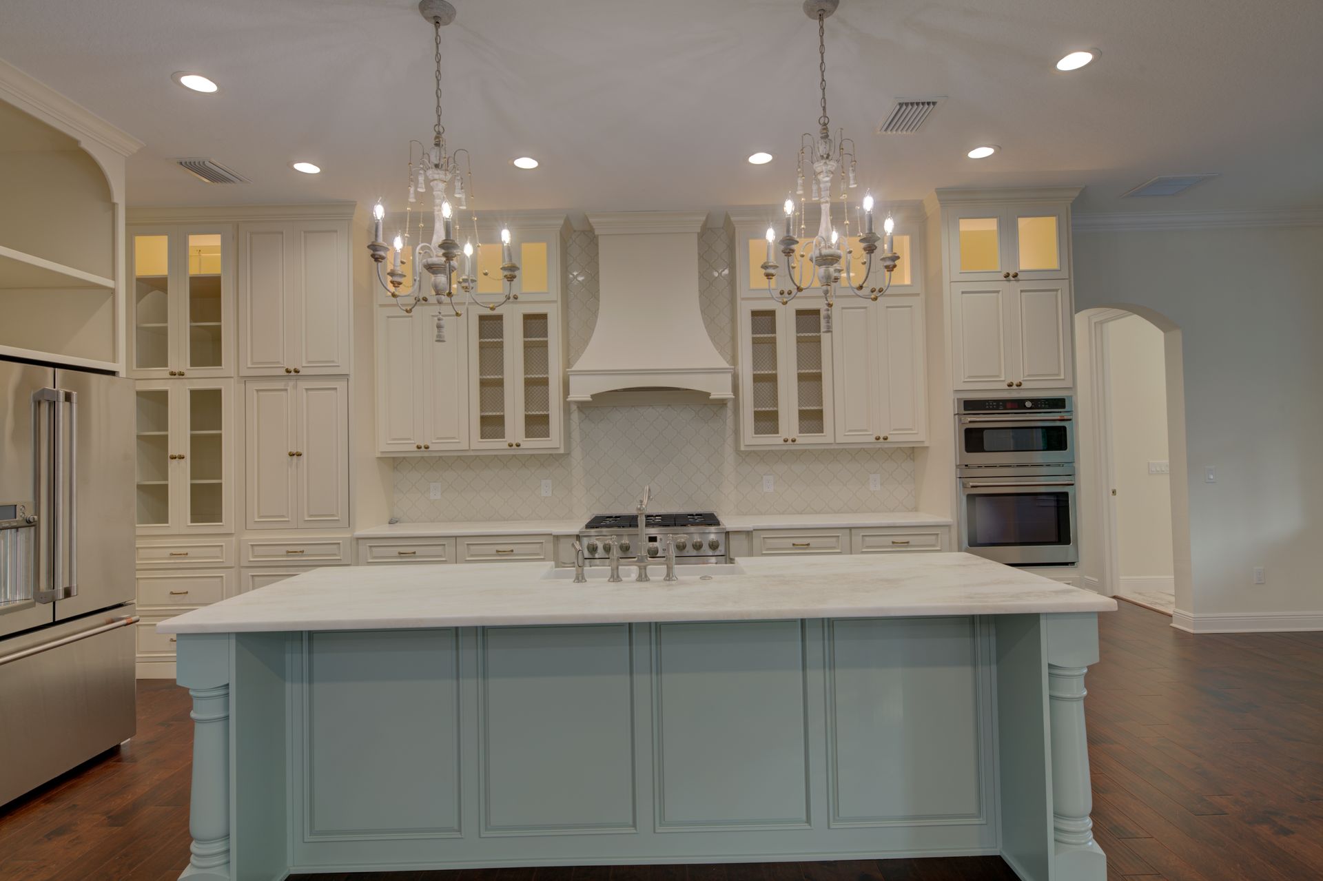 Spacious white kitchen with island, cabinets, chandeliers, and stainless steel appliances.