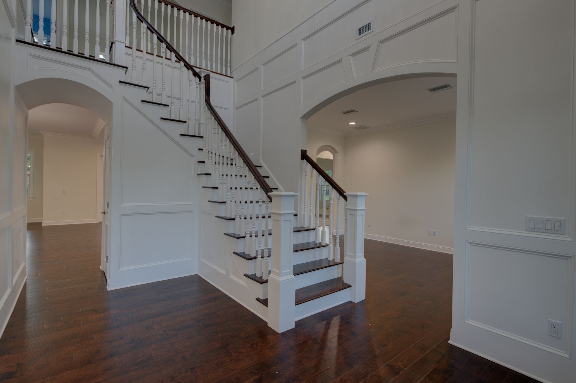 Grand foyer with white walls, dark wood floor, and a staircase.