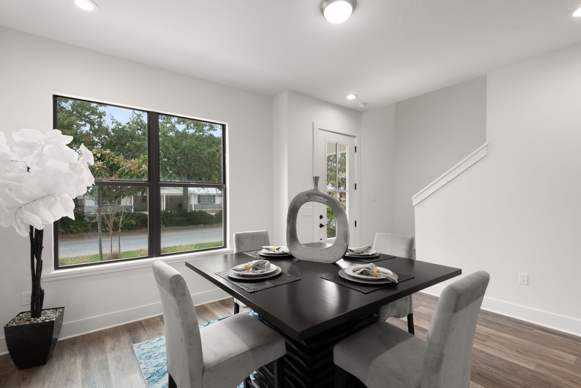 Dining room: square black table, four light gray chairs, large window, decorative vase, white walls.