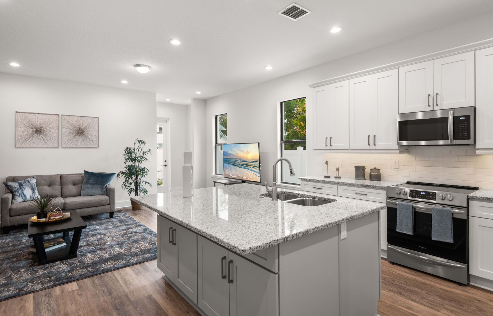 Open-concept kitchen and living area with a gray island, white cabinets, and a gray sofa.