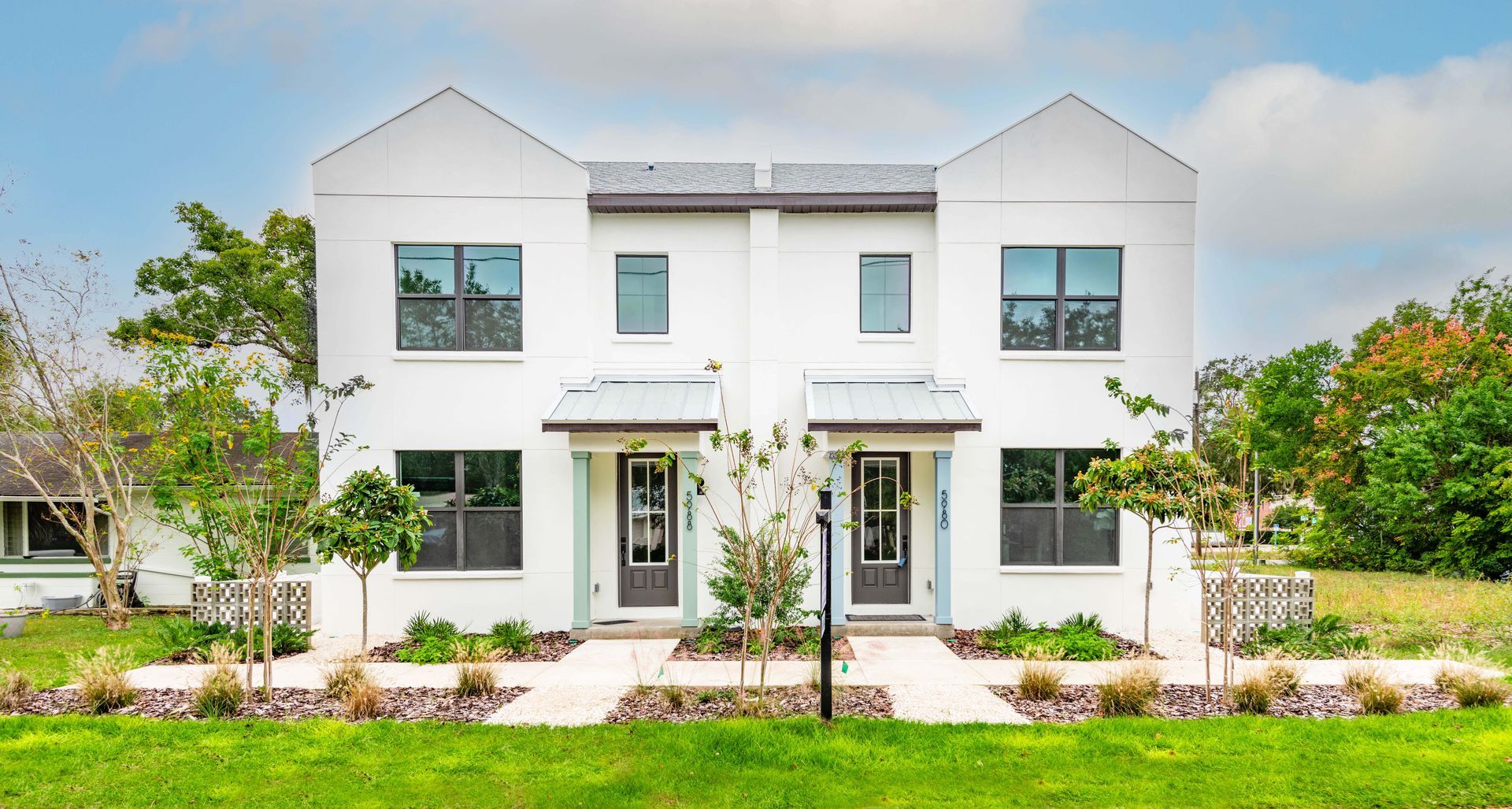 White townhouses with black framed windows and doors; green lawn, blue sky.