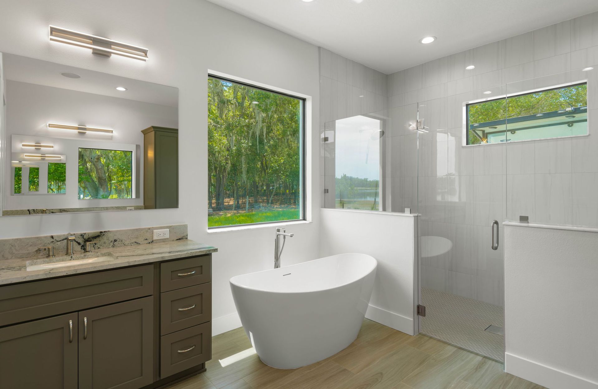 Modern bathroom with a freestanding tub and a large window overlooking greenery.