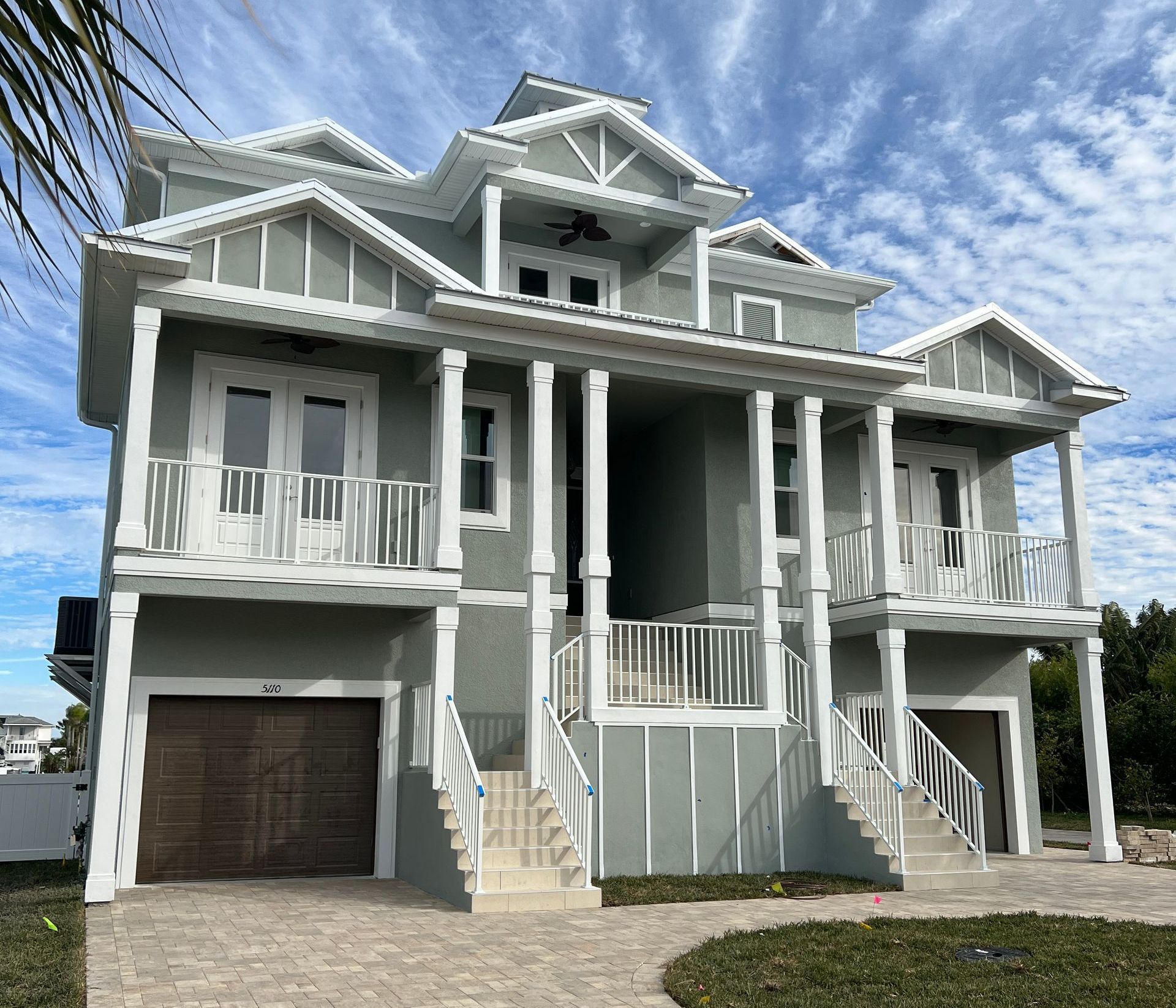 Multi-story coastal home with gray siding, white trim, and balconies under a blue sky.