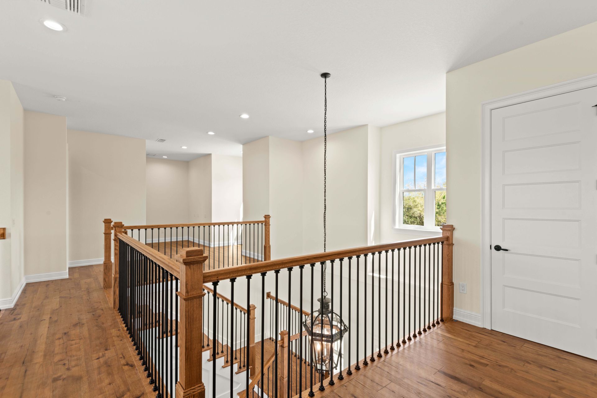 Interior hallway with wooden floors, railings, and a hanging light fixture.