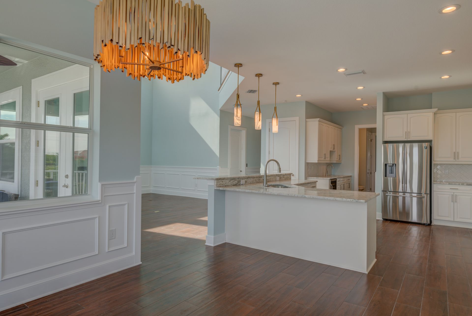 Open kitchen with hardwood floors, white cabinets, and a stainless steel refrigerator.