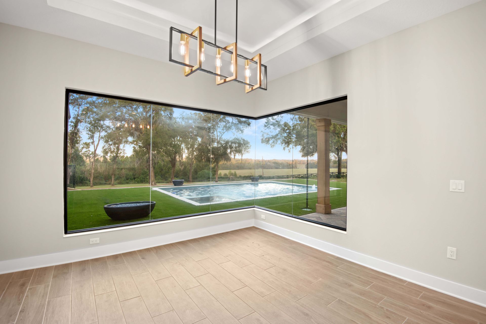 Empty room with large corner window overlooking a pool and backyard.