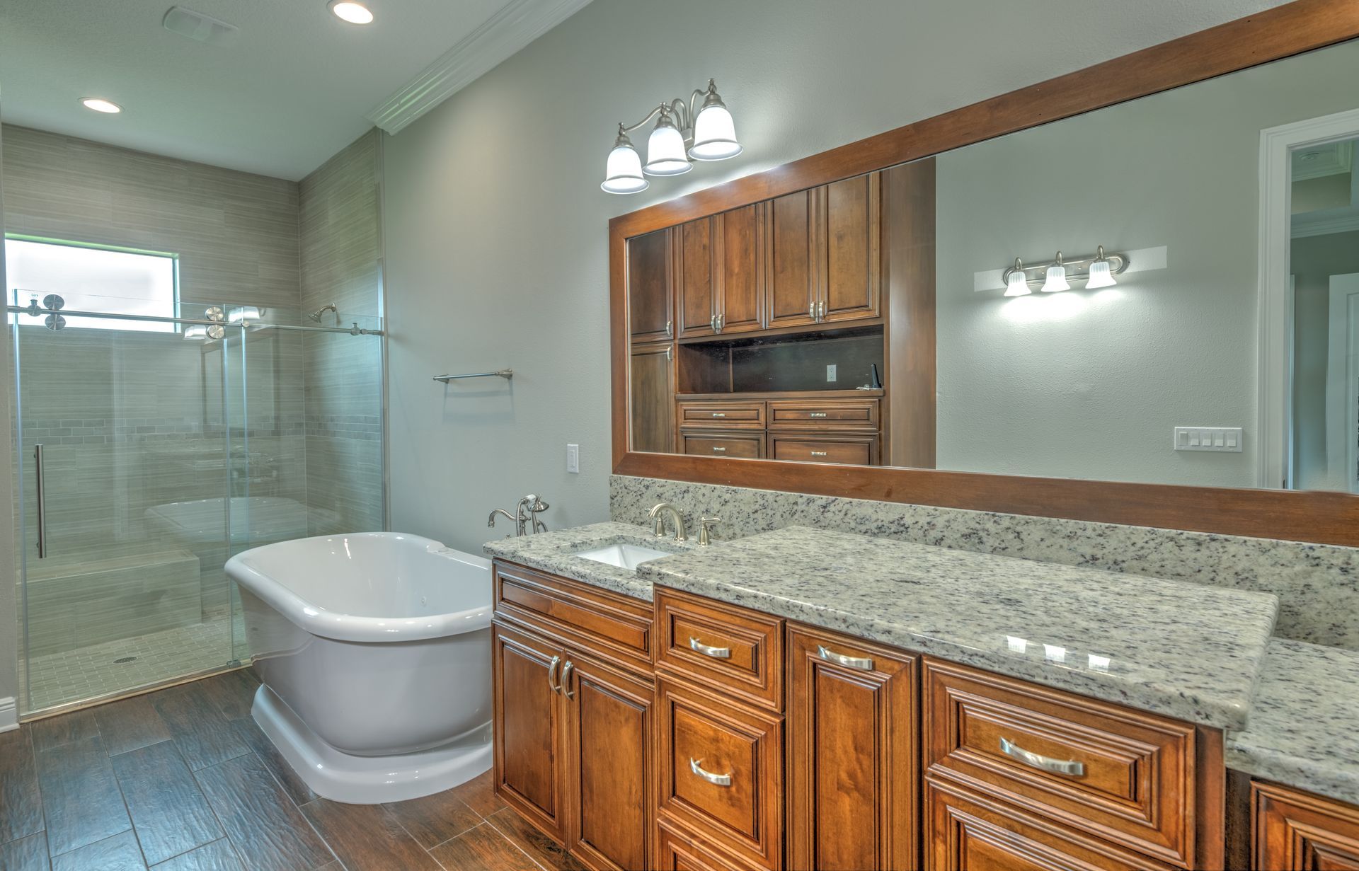Bathroom with wooden cabinets, granite countertop, bathtub, and walk-in shower.