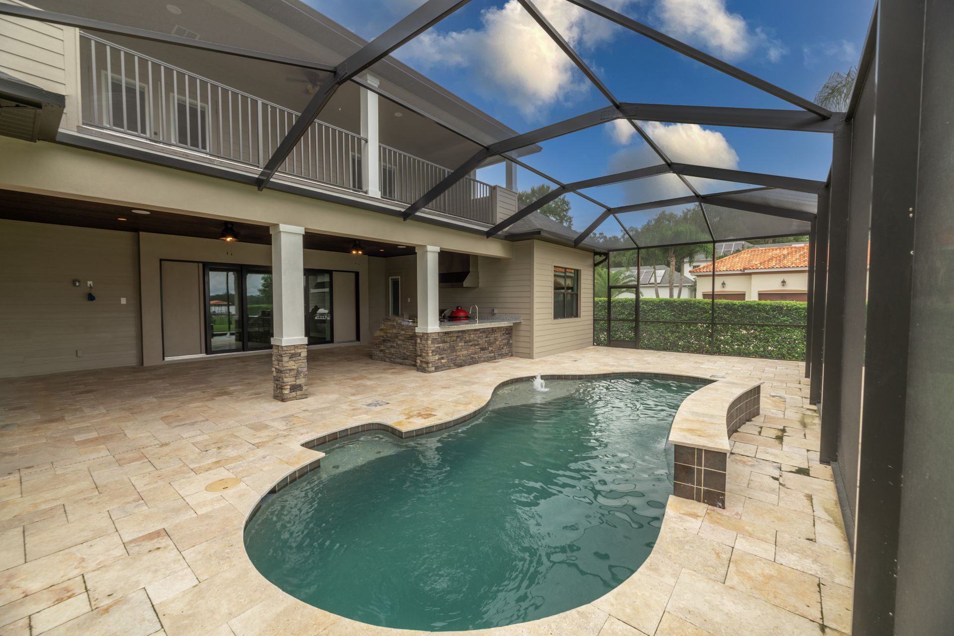 Swimming pool enclosed in a screened patio, adjacent to a two-story beige house with a balcony.