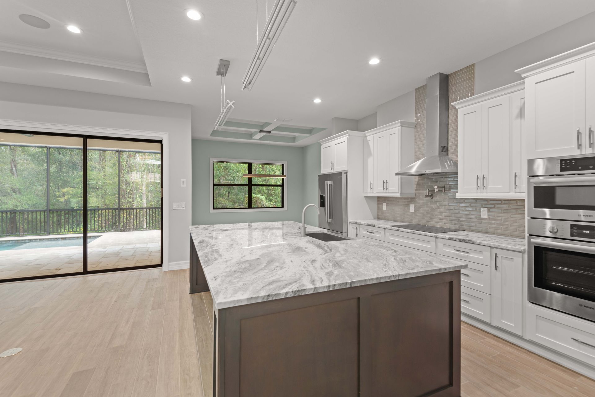 Modern kitchen with white cabinets, dark island, and sliding doors to pool.