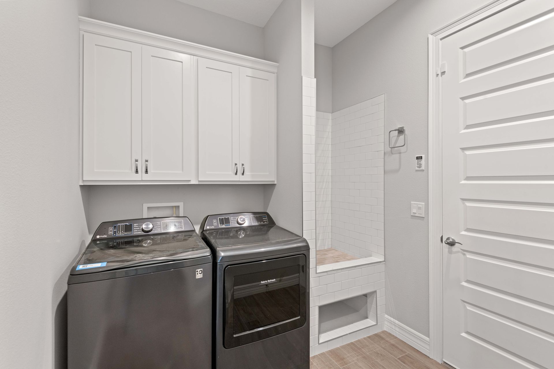 Laundry room with white cabinets, a washer, and dryer, and a white tiled nook with a bench.