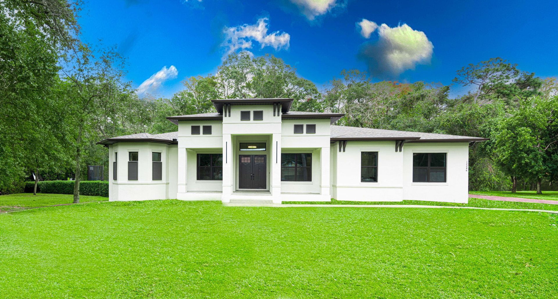 White house with dark windows and door on green lawn under blue sky, trees in background.