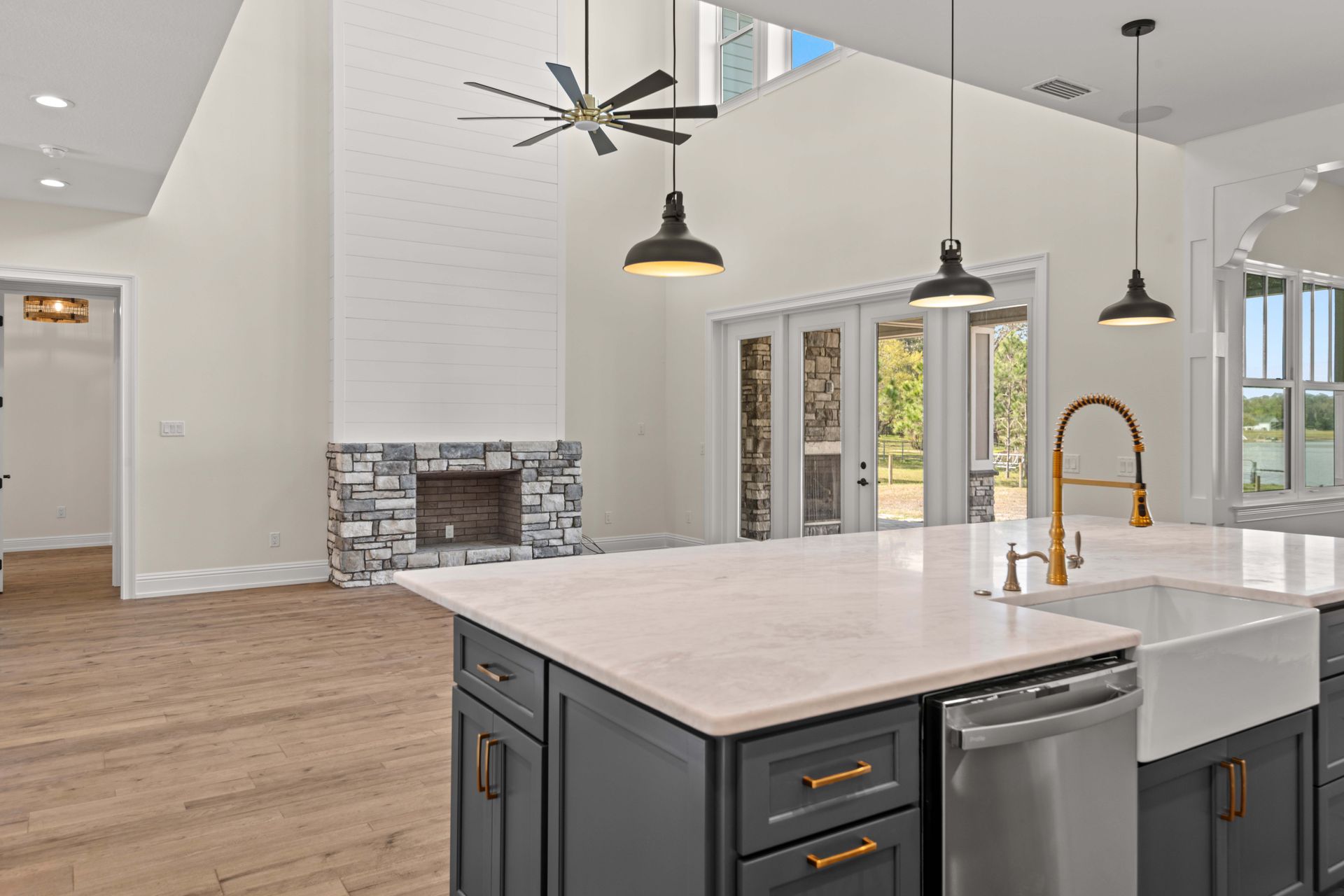 Modern kitchen with island, fireplace, and glass doors. Light wood floors, white walls, dark cabinets, and pendant lights.