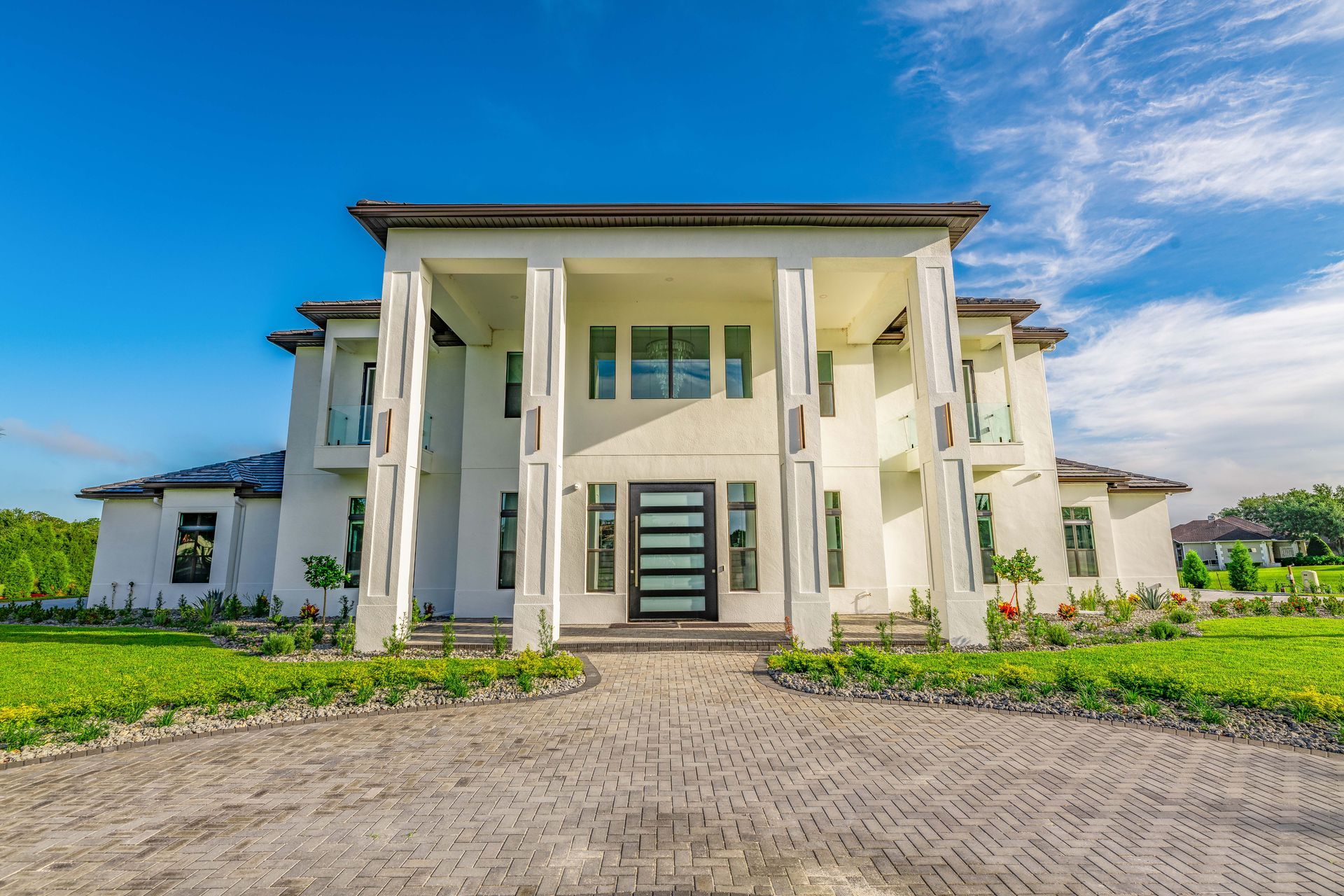 White mansion with large columns, blue sky, and brick driveway.