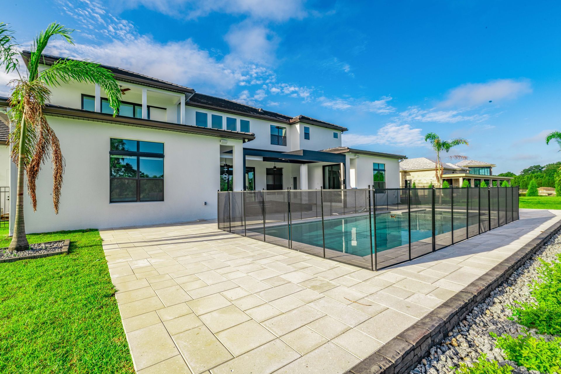 Luxury home with a pool fenced in by a mesh barrier, green grass, and clear blue sky.
