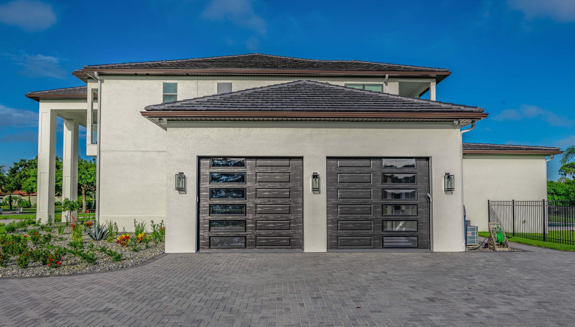 Two-story stucco house with gray garage doors, driveway, and blue sky.