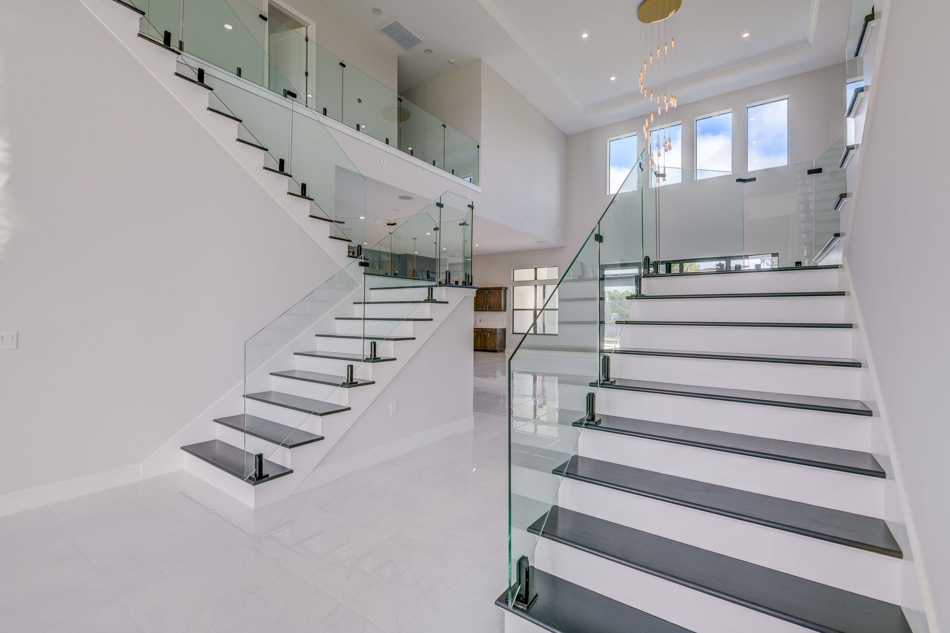 Bright white interior with a modern staircase featuring glass railings and black steps.
