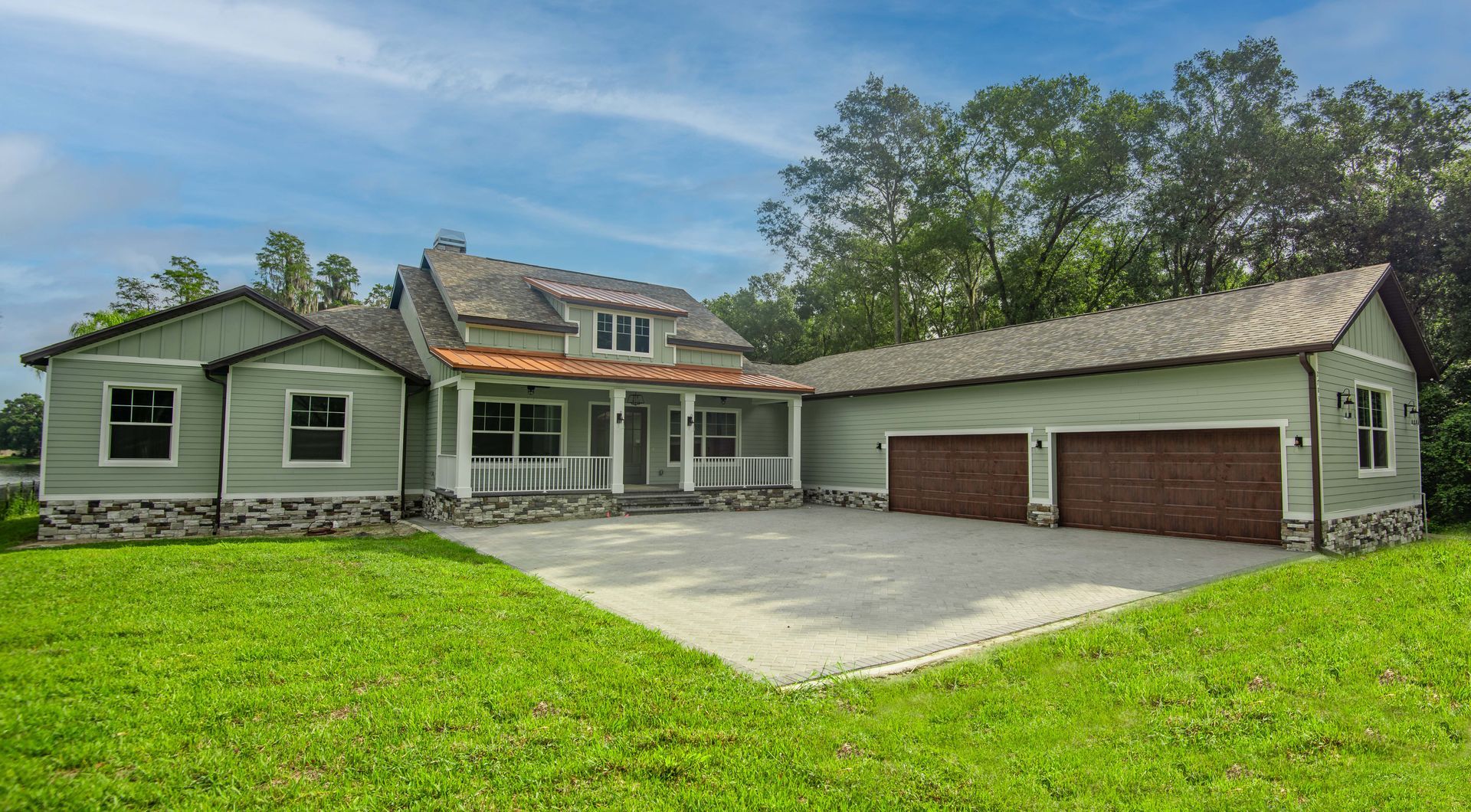 Green house with stone accents, a porch, and a two-car garage, on a grassy lot.