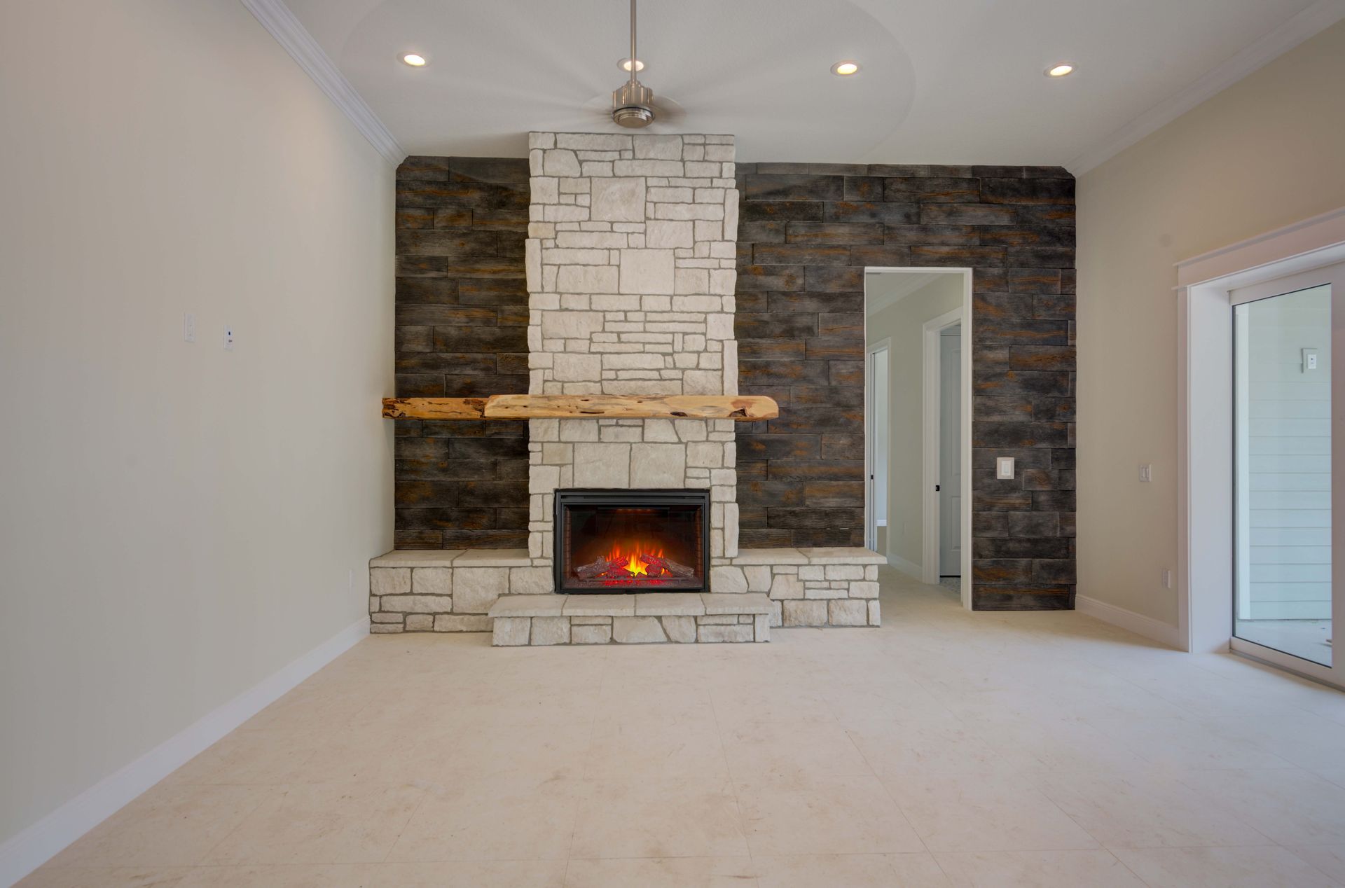 Empty room with fireplace, white walls, stone facade, wooden mantel, and dark accent wall.