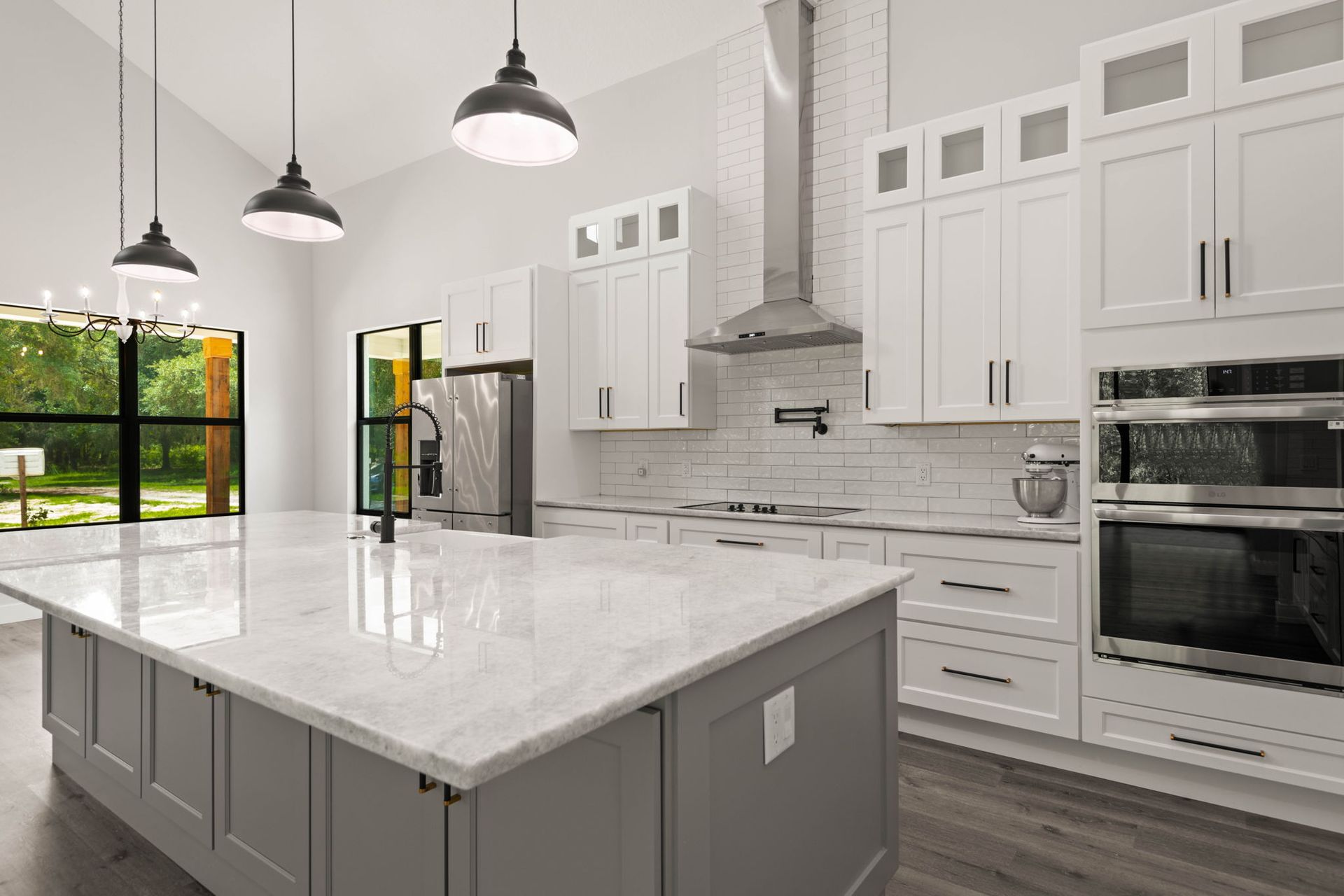 Modern white kitchen with gray island, stainless steel appliances, and pendant lights.