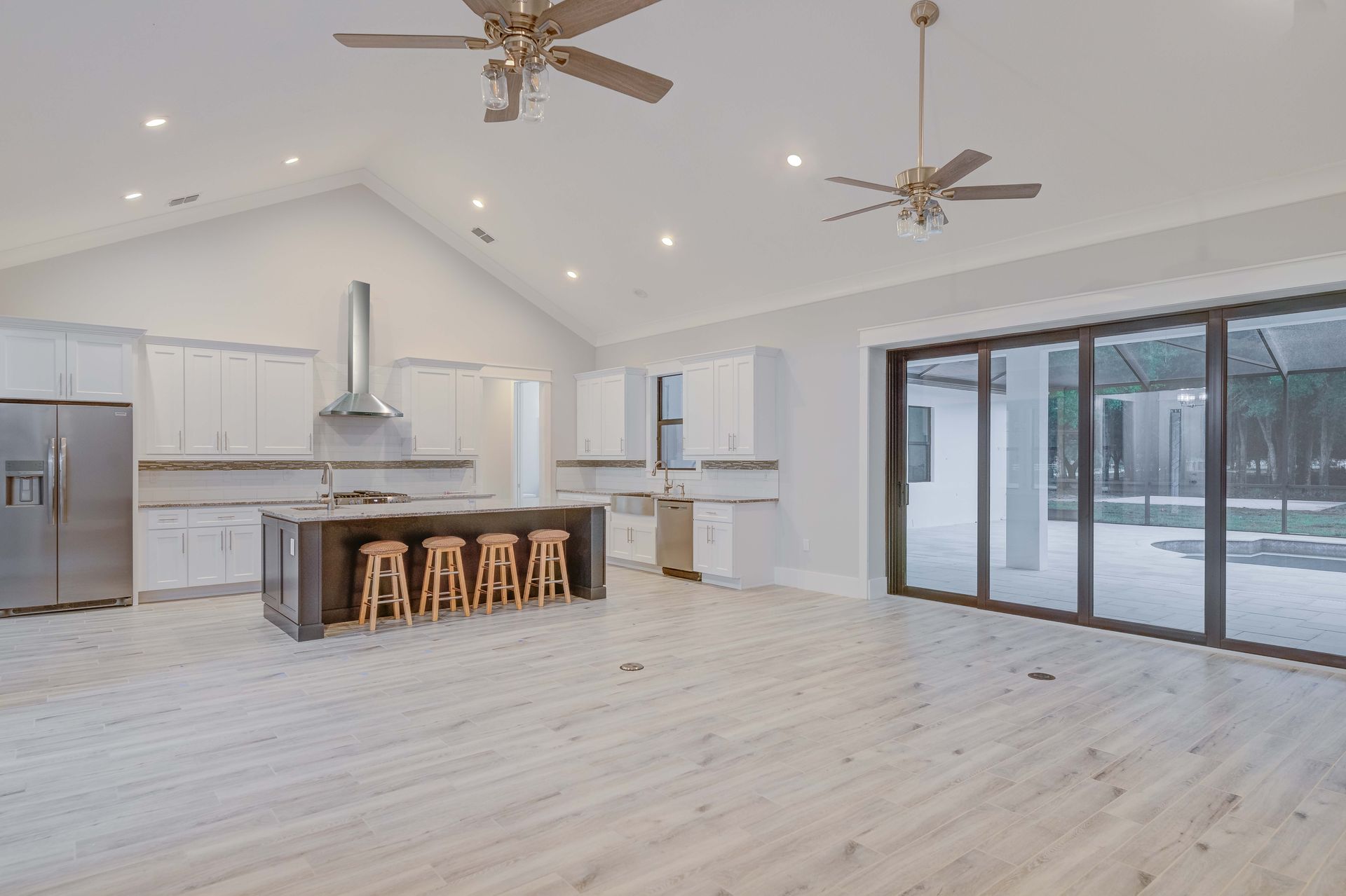Open concept kitchen with white cabinets, dark island with stools, and large sliding doors to a pool.