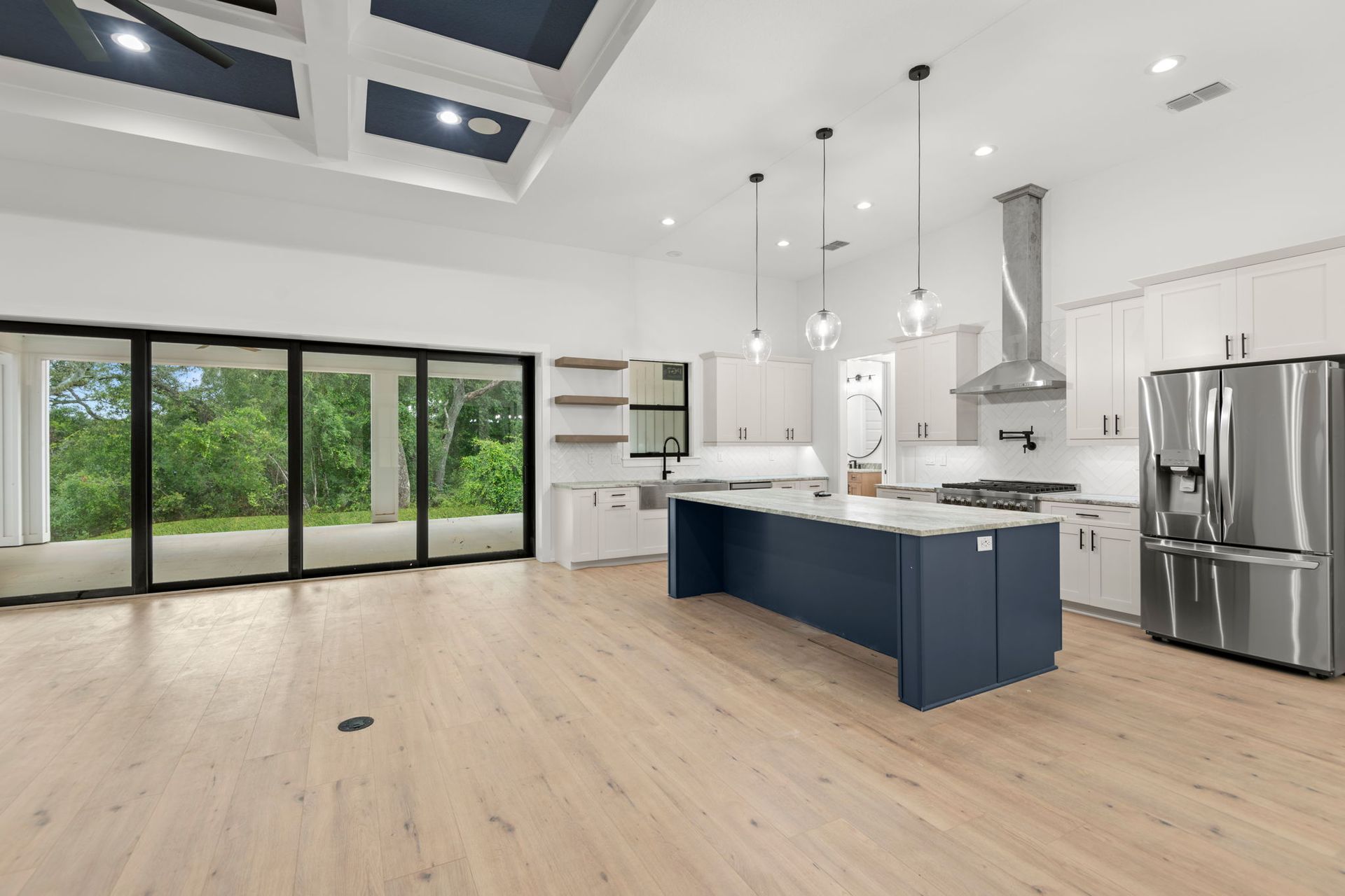 Modern kitchen with blue island, white cabinets, stainless steel appliances, and large glass doors.