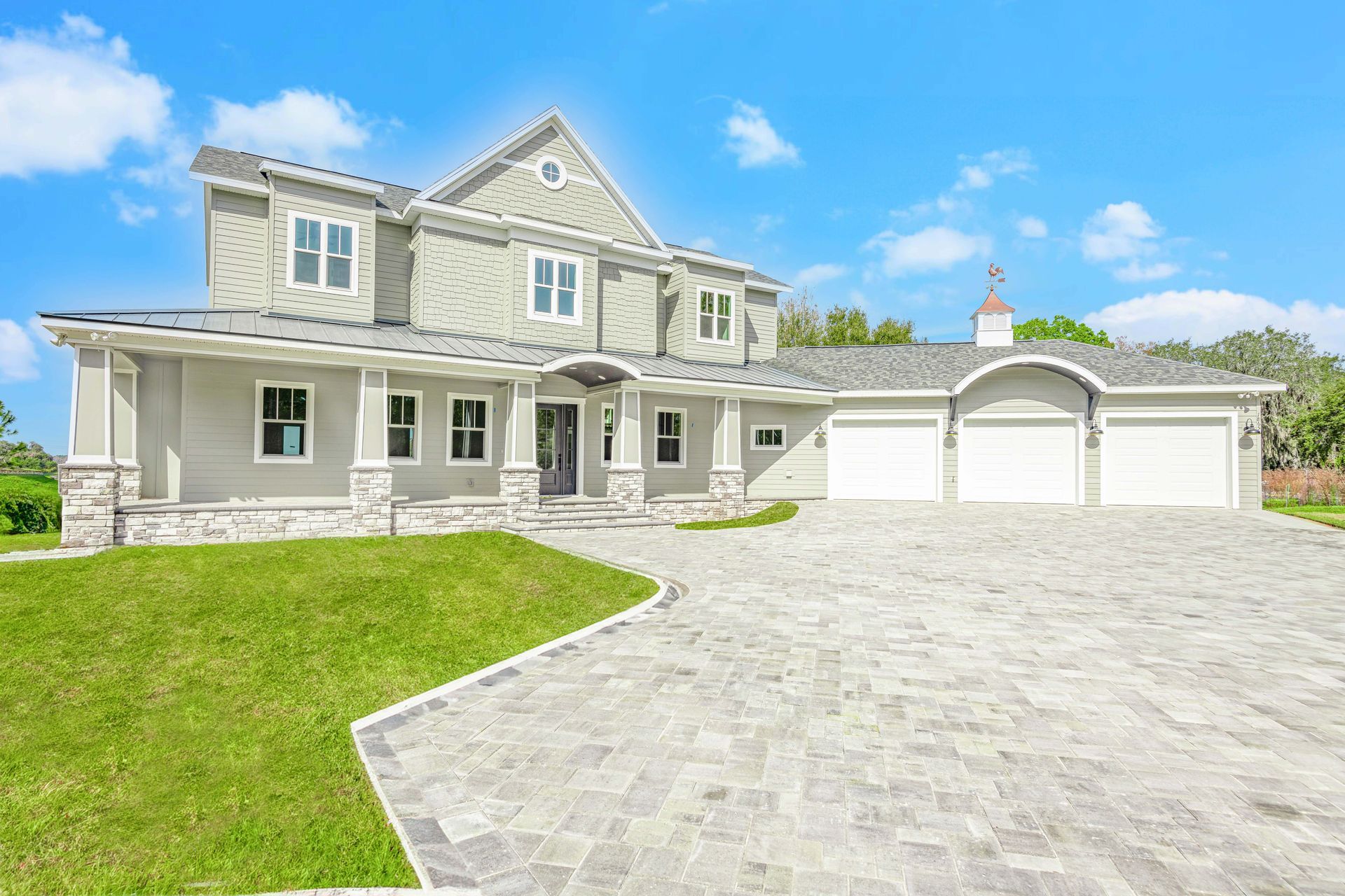 Two-story gray house with a paved driveway and three-car garage under a blue sky.