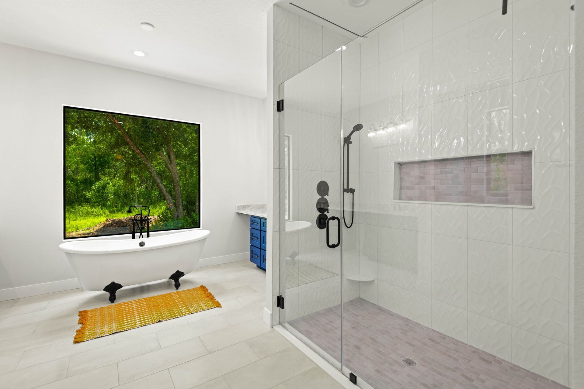 Bathroom with a claw-foot tub by a window overlooking a tree, shower with white tiled wall, and blue vanity.