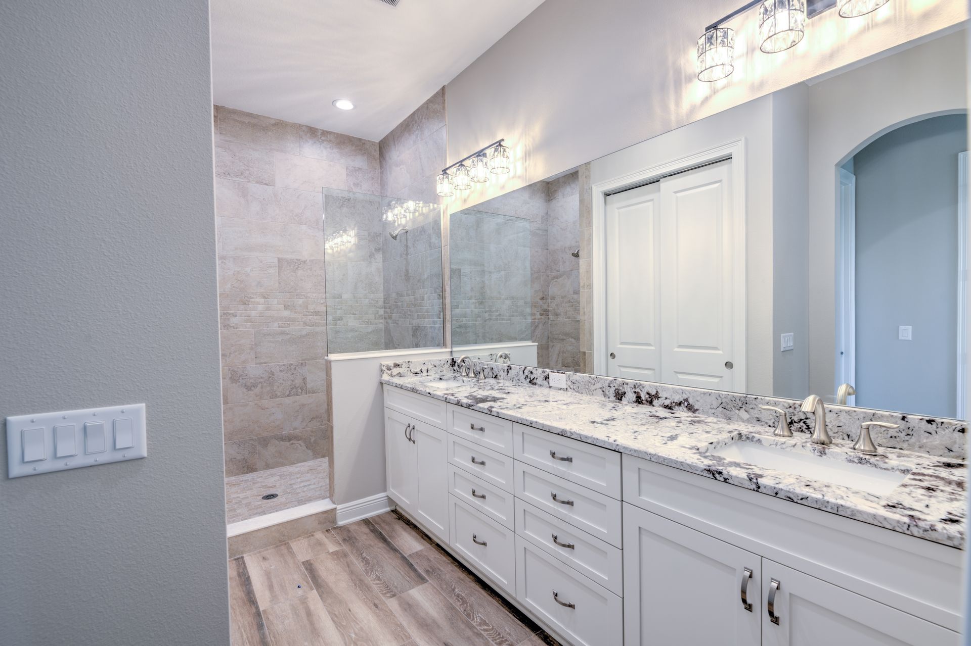 Bright, modern bathroom with glass shower, double vanity, and large windows. White and gold accents.