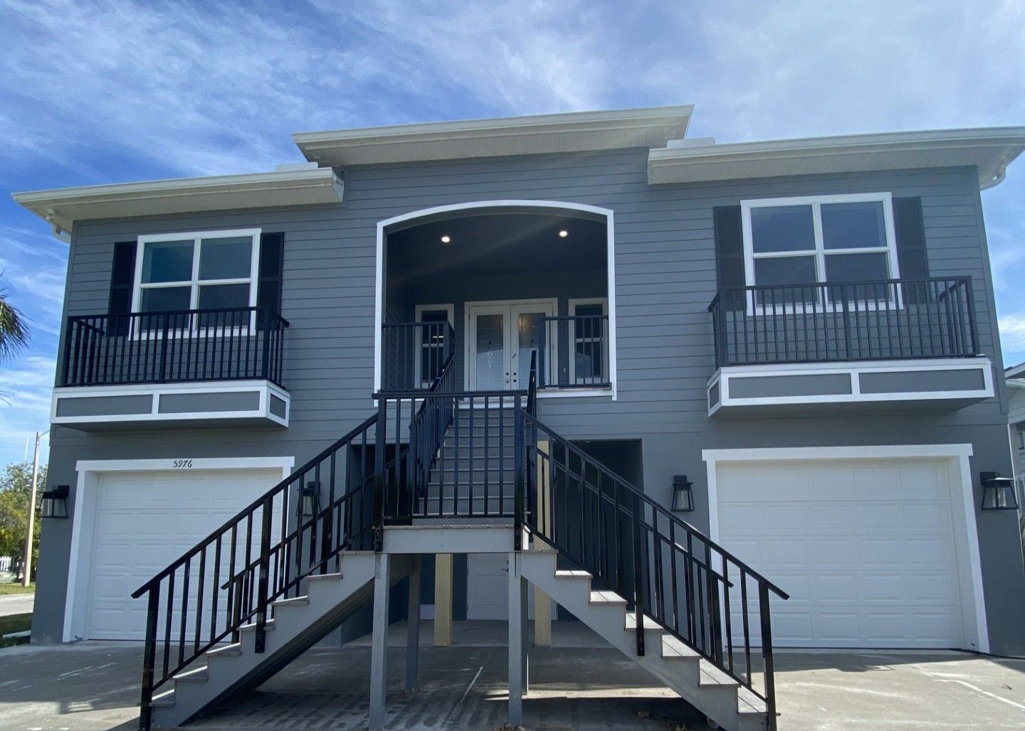 White farmhouse with a long porch, three dormers, and a green lawn under a colorful sunset.