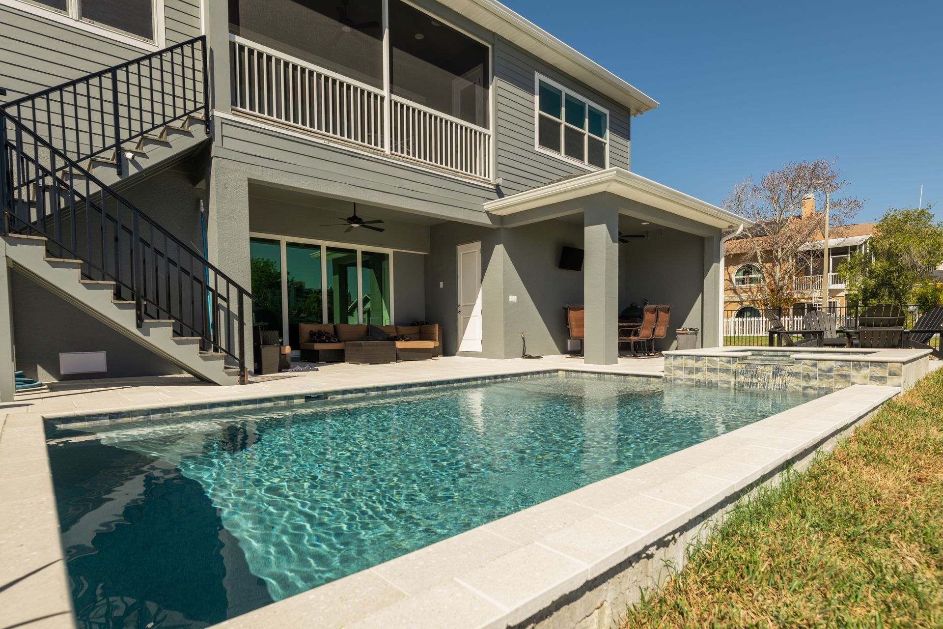 A modern gray two-story house with a backyard swimming pool, patio, and outdoor staircase.