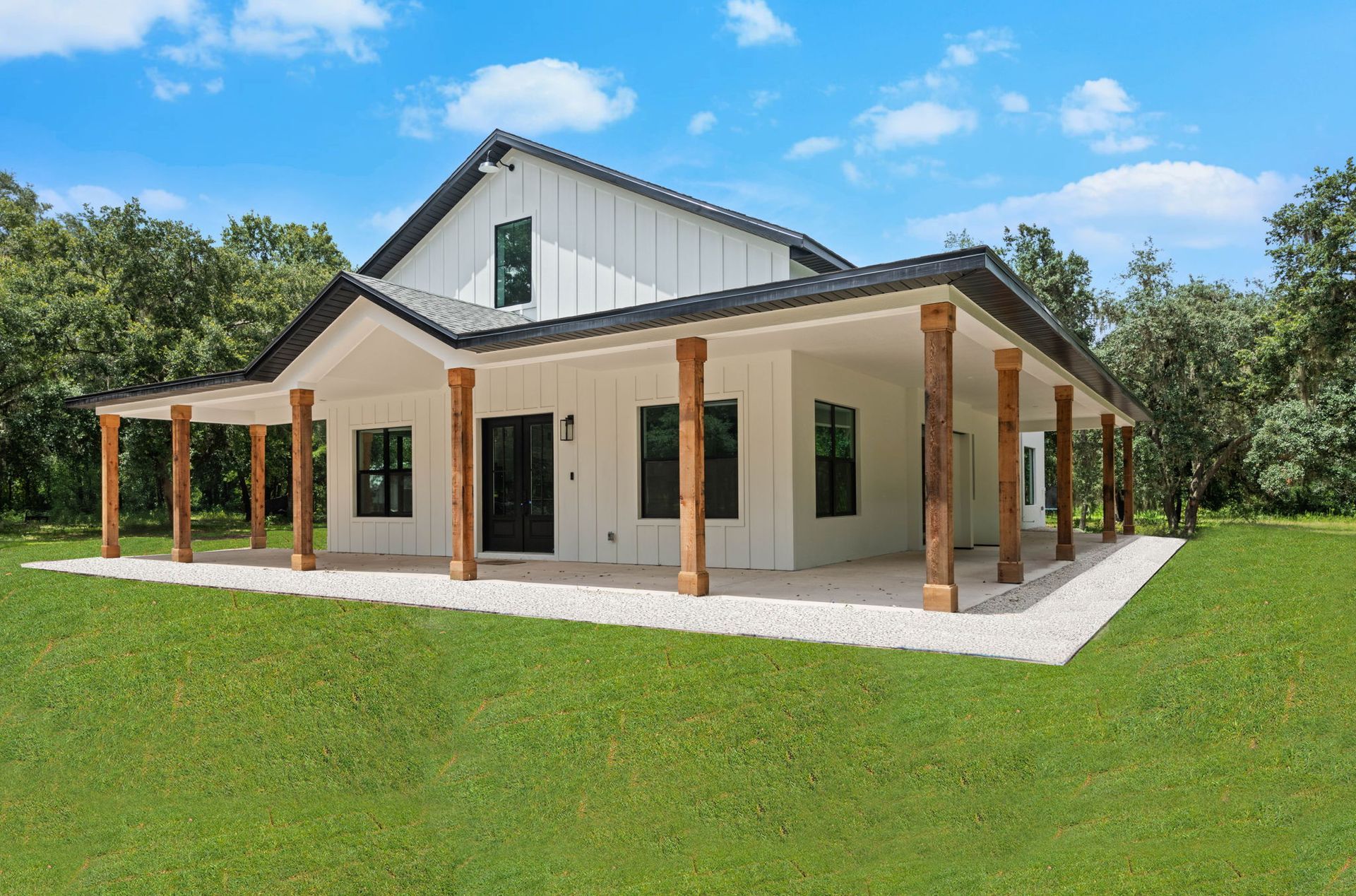 White farmhouse with a wraparound porch, wooden posts, and a dark roof, set on a green lawn.