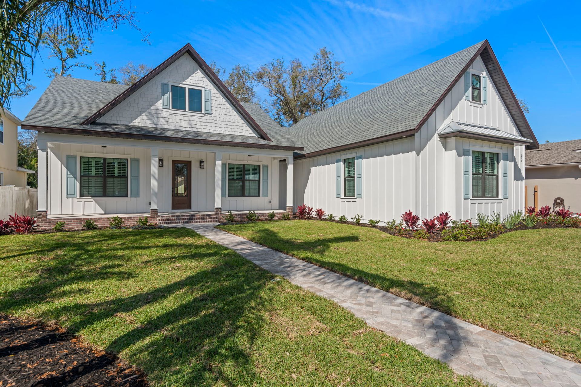 White farmhouse with gray roof, blue shutters, and a stone path leading to the front door.