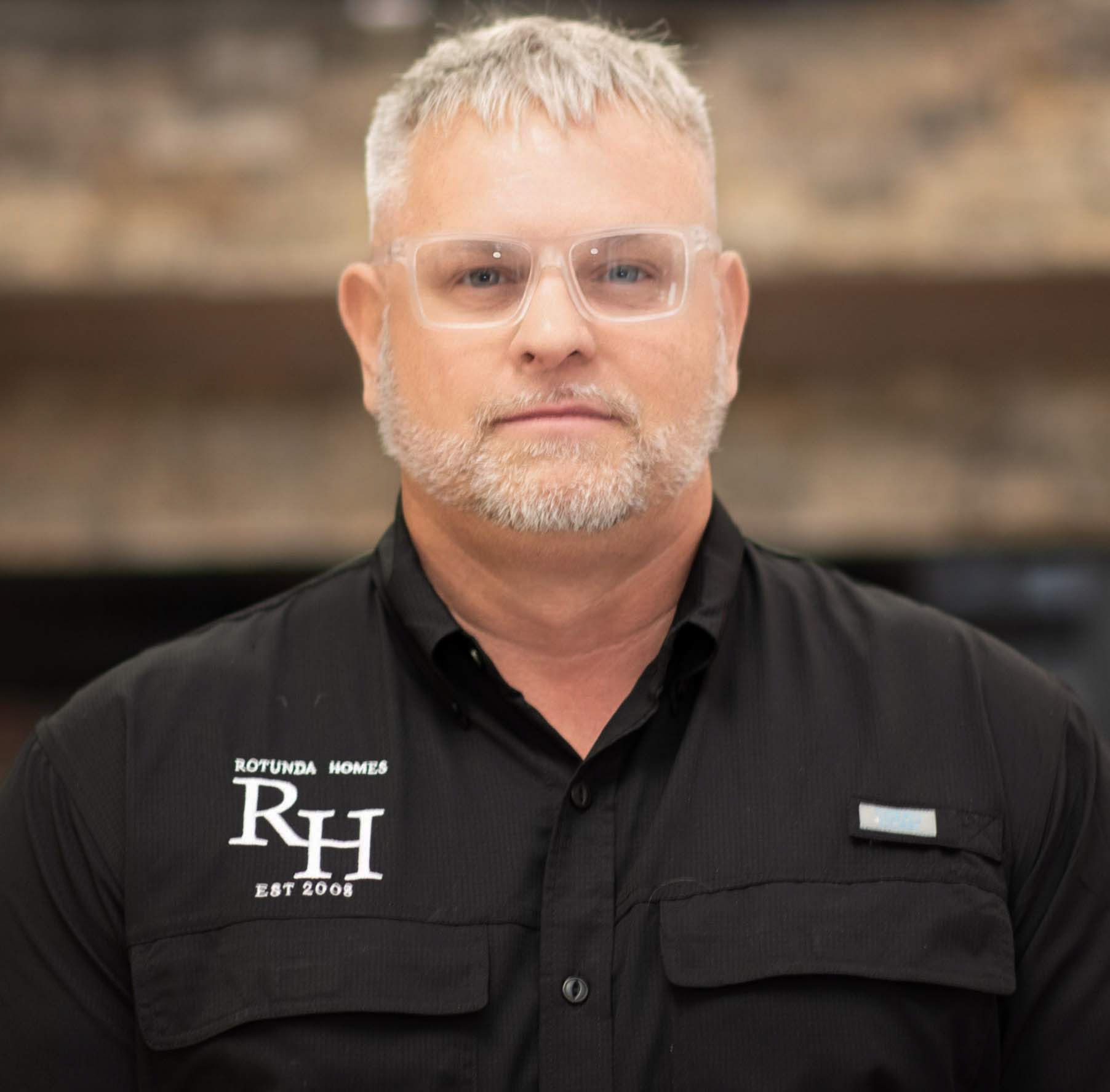 Man with gray hair and beard wearing glasses and a black shirt with logo.