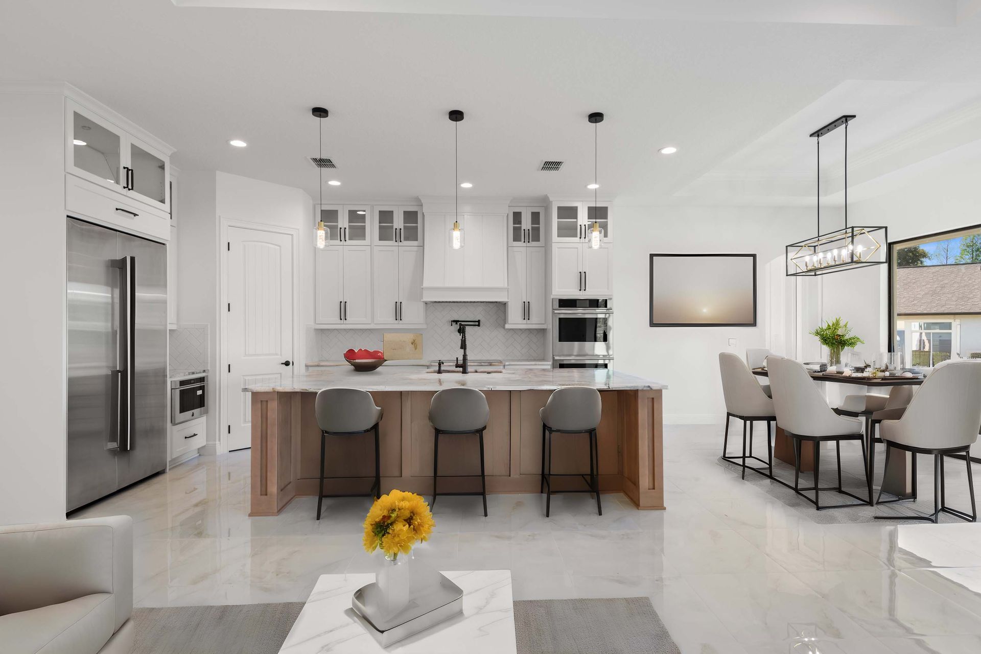 Spacious kitchen with island, pendant lights, large windows overlooking a backyard and a fireplace on a black wall.
