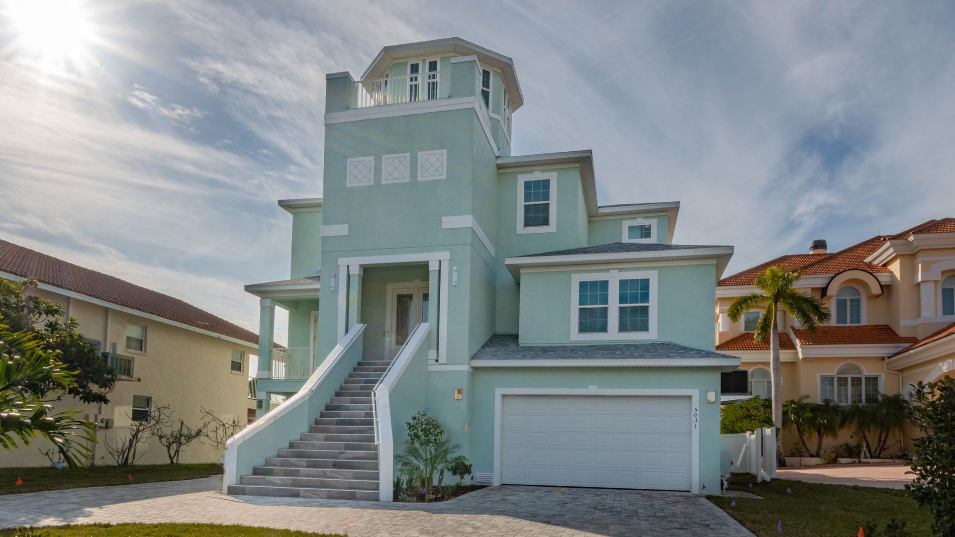 White farmhouse with a wraparound porch, wooden posts, and a dark roof, set on a green lawn.