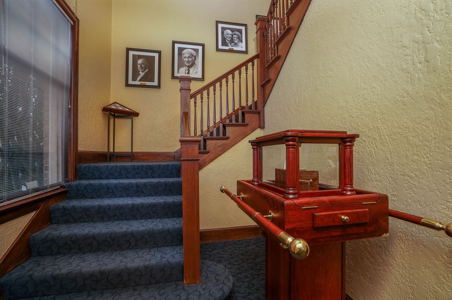 A staircase with blue carpet and a wooden box on the bottom of the stairs.